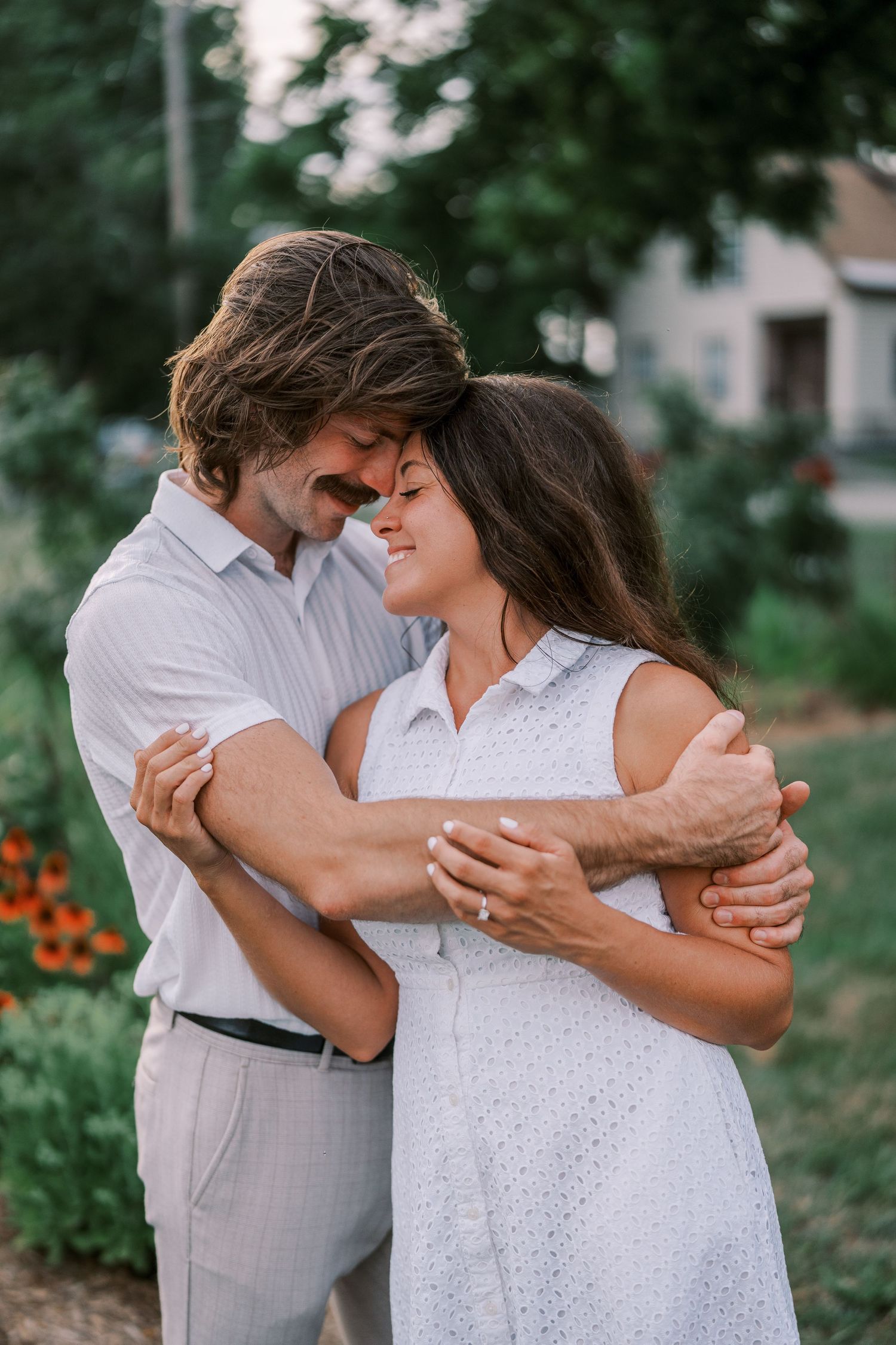A couple embraces tenderly in a garden setting wearing coordinating white outfits.
