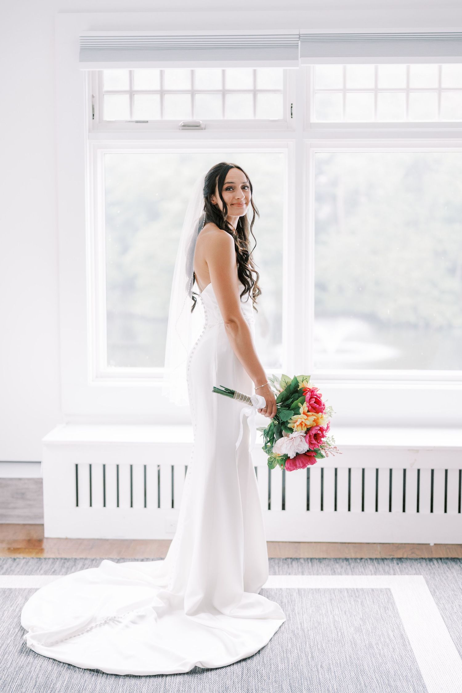 A person in a flowing white wedding gown holds a vibrant bouquet in a bright, modern space.