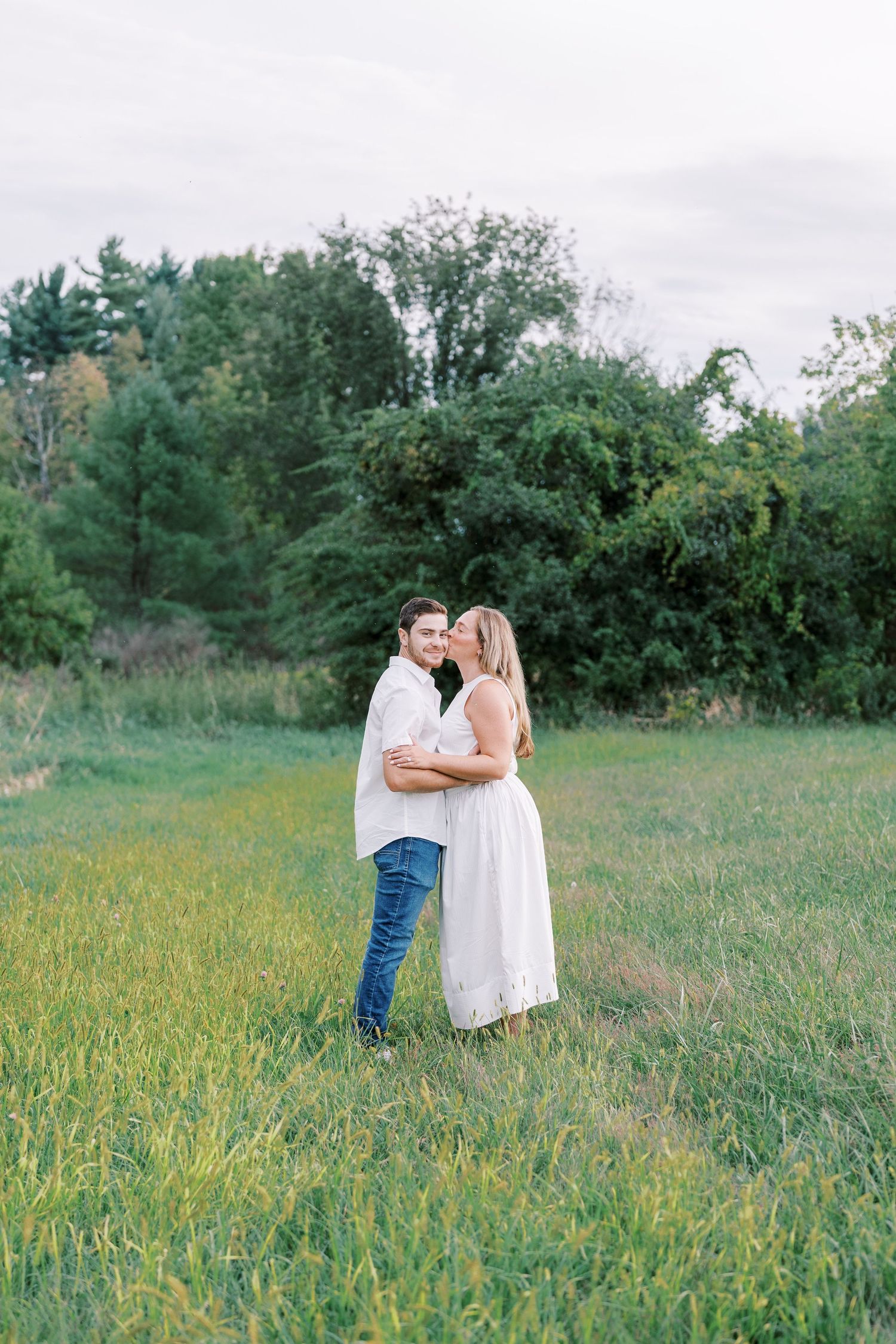 A couple embracing in a sunlit meadow surrounded by wildflowers and greenery.