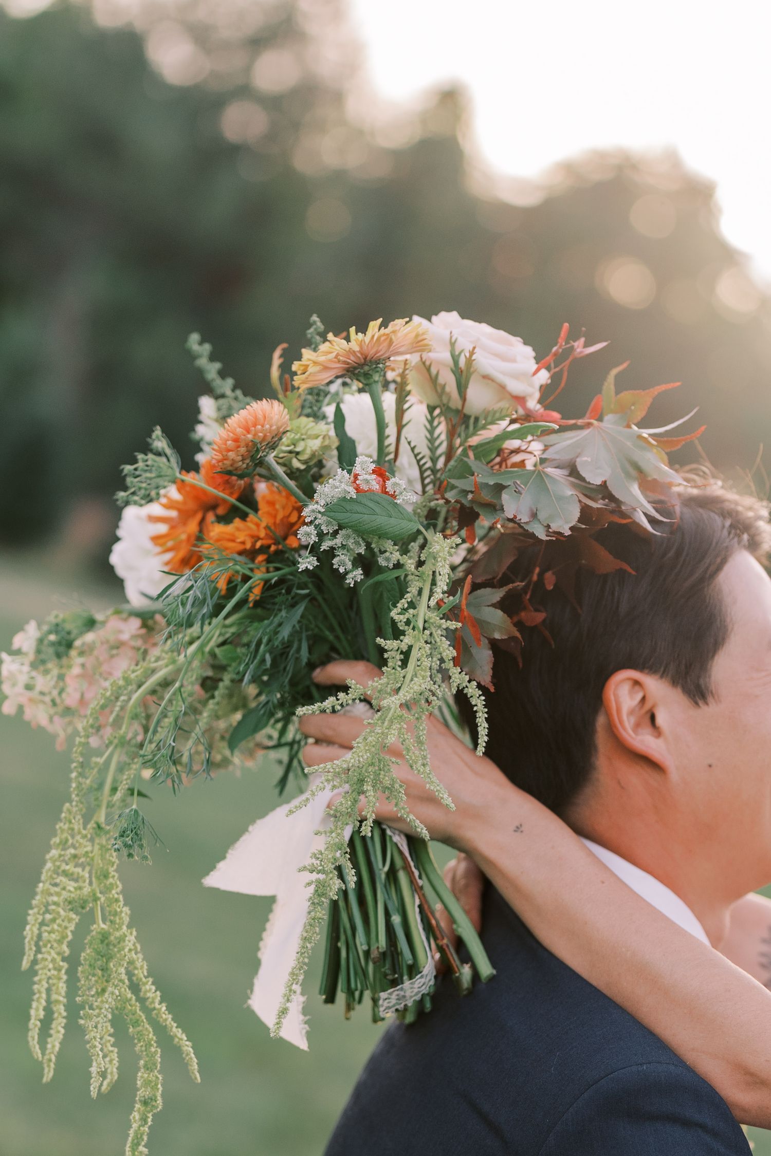 Wedding couple's floral crown details with orange blooms and greenery at sunset.