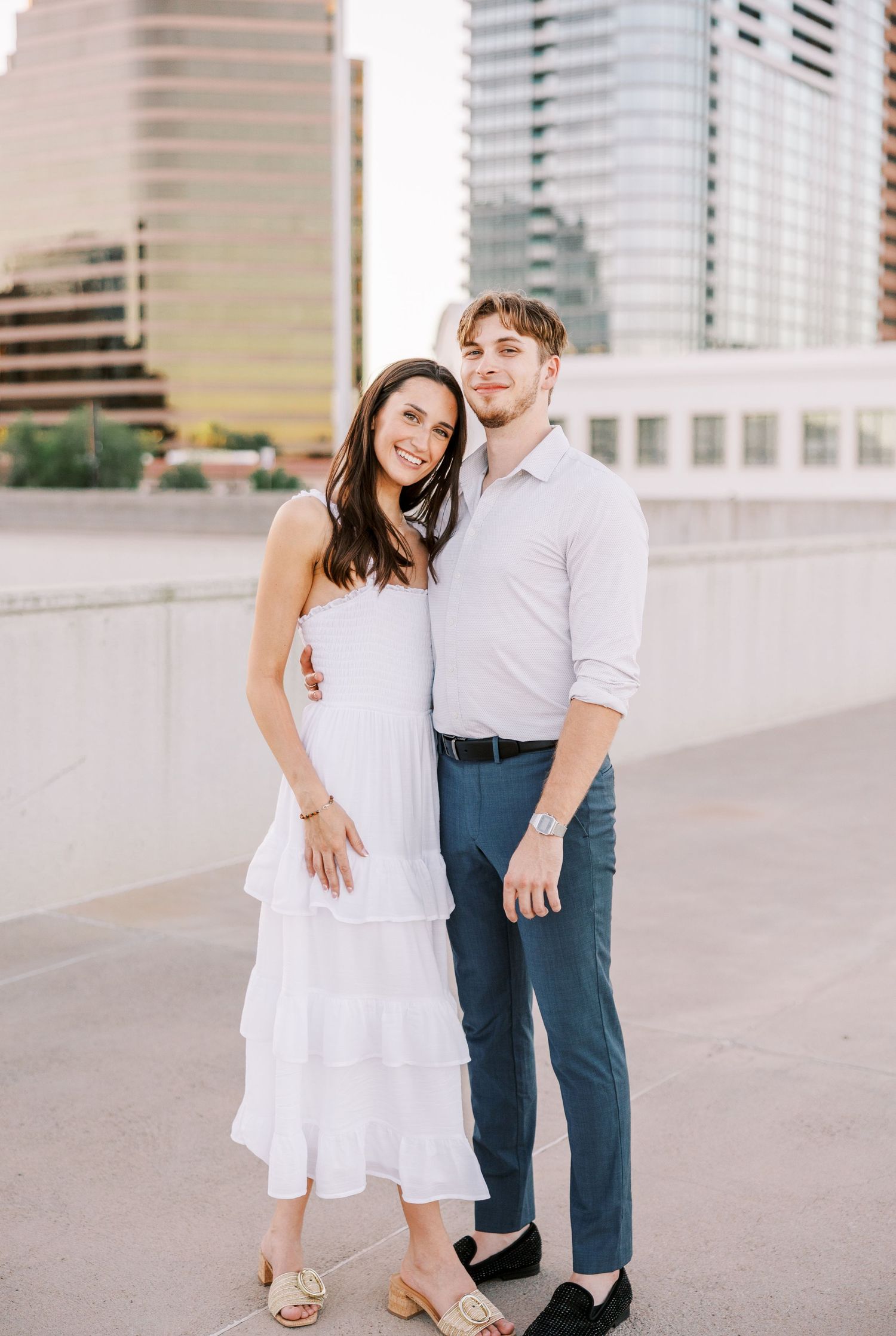 Stylish couple poses together on an urban rooftop with city buildings visible in the background.