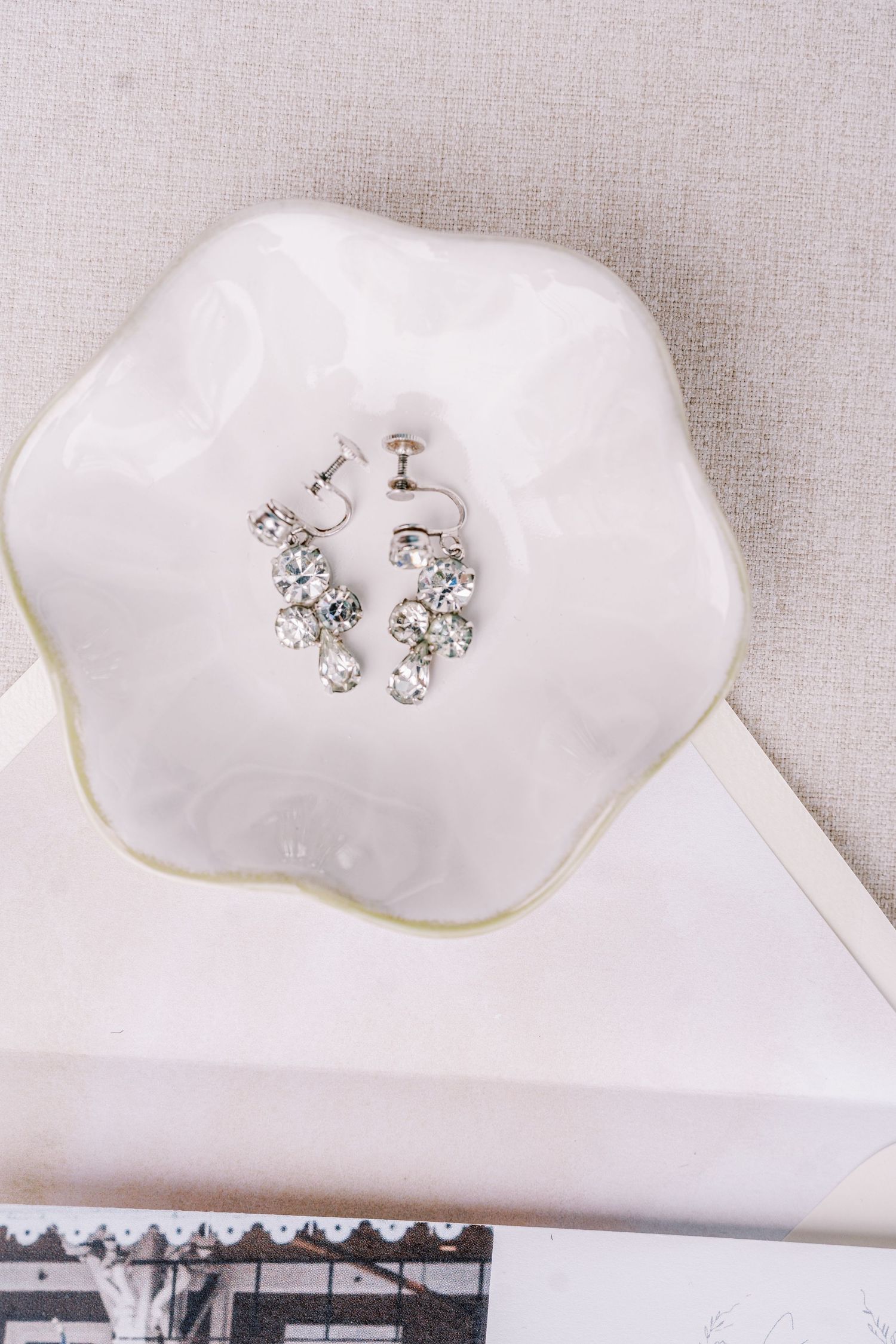Delicate crystal earrings displayed on white fabric surfaces.