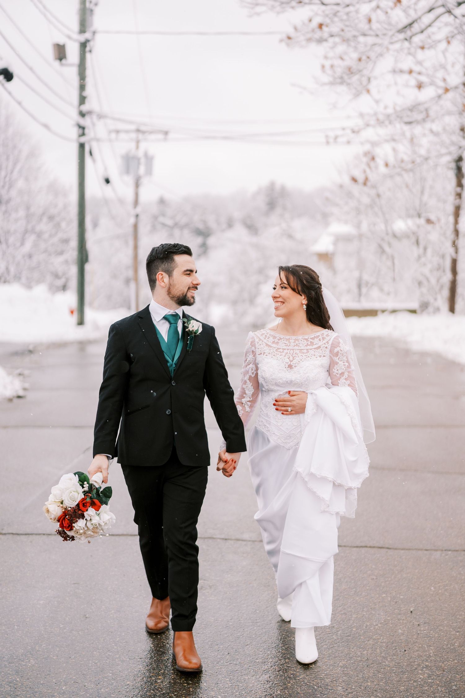 Couple walking hand in hand on snowy street during winter wedding.