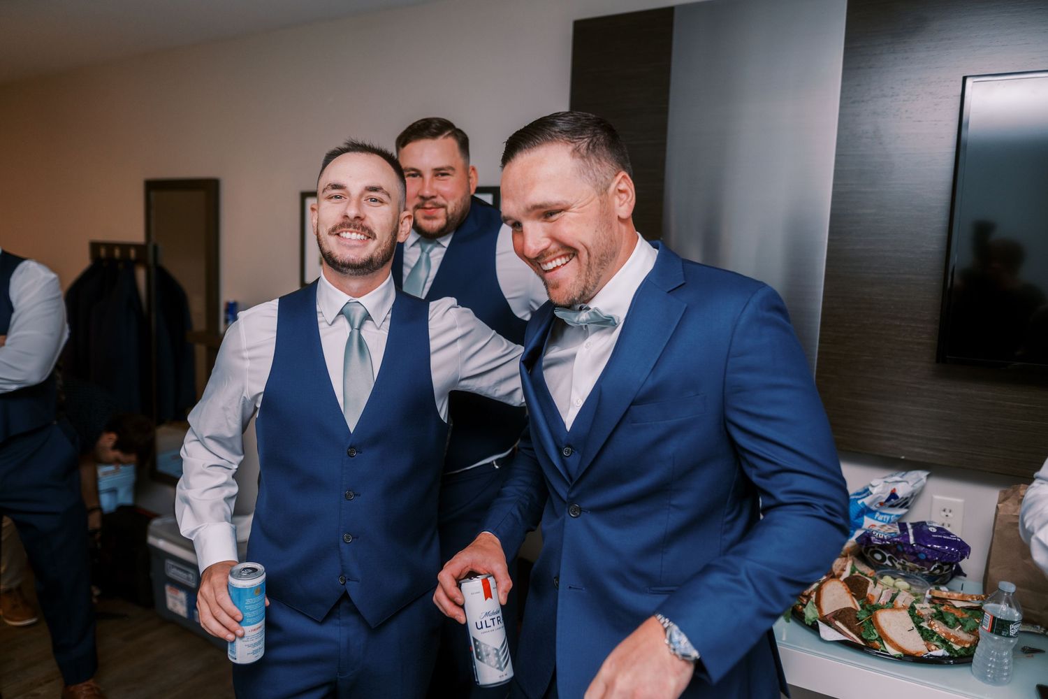 A group in formal attire laughs and socializes at an indoor gathering wearing navy suits.