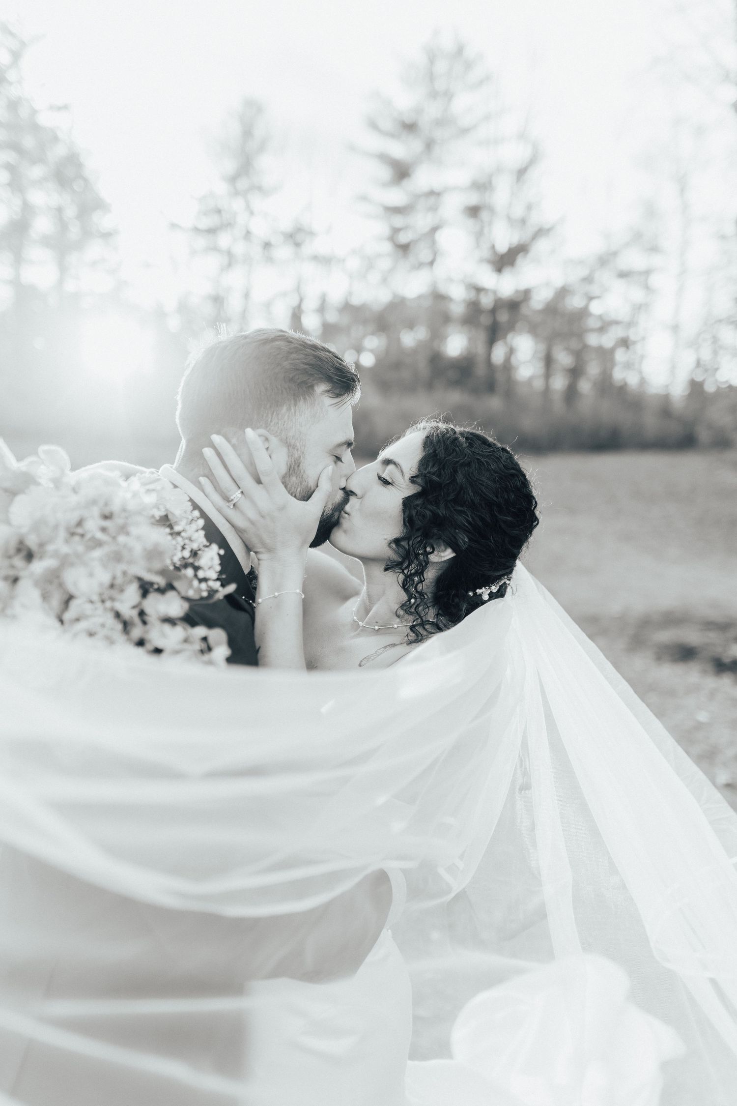 A romantic black and white wedding photo series showing a couple embracing with flowing white veil creating ethereal movement.
