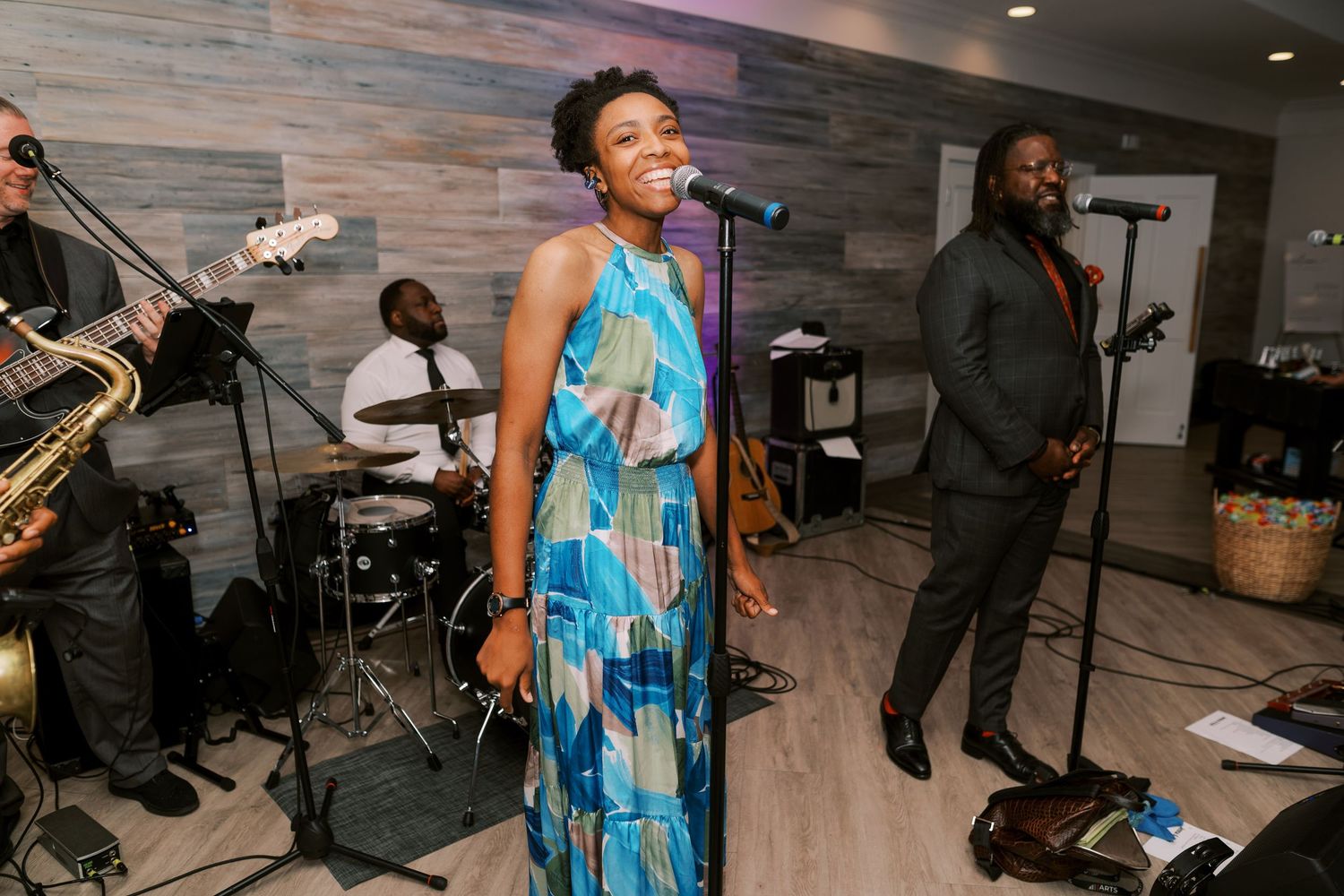 A singer in a blue and white dress performs with a live band on stage in a modern venue.