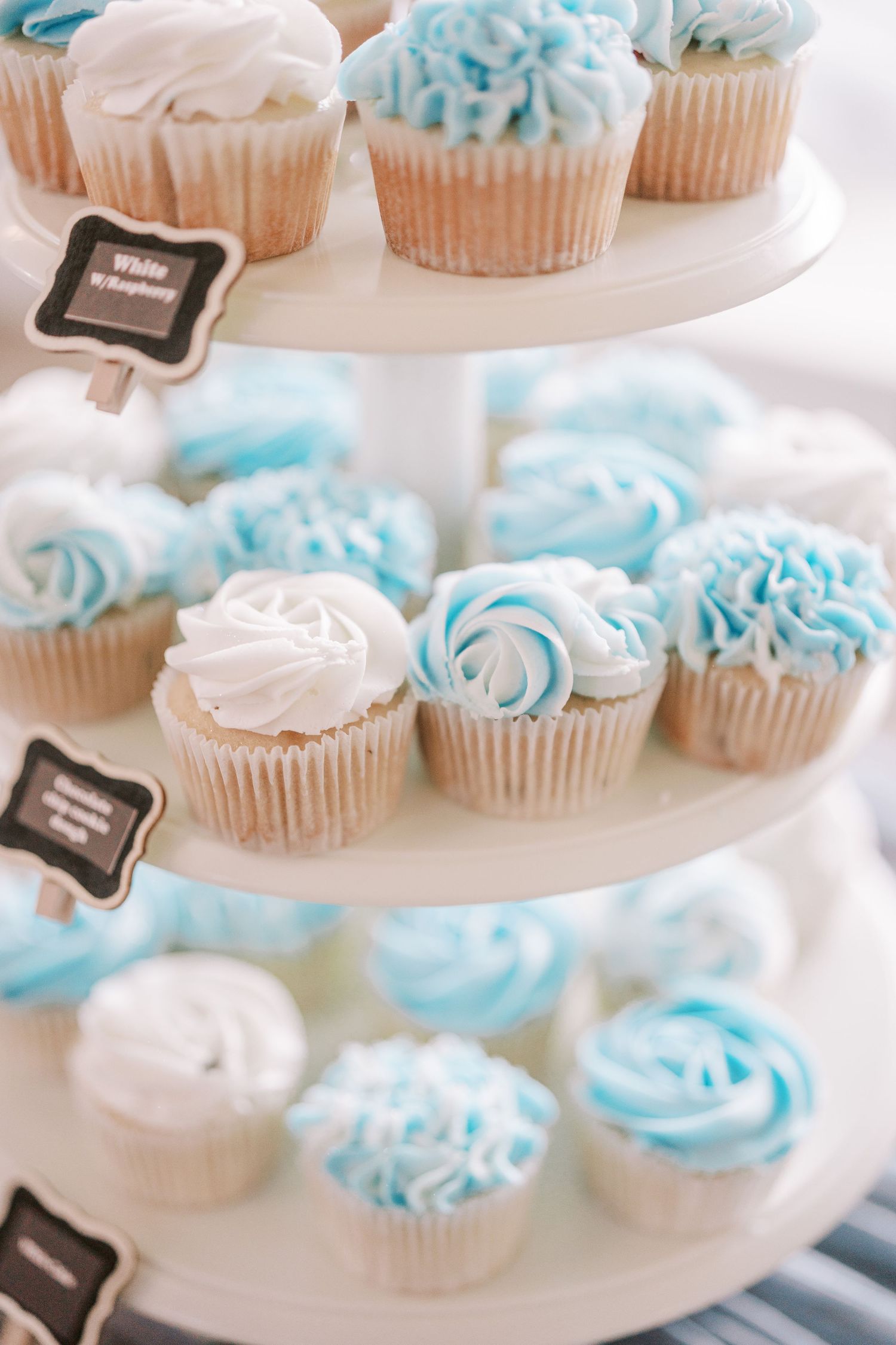 White and light blue frosted cupcakes arranged on a tiered dessert stand for an elegant party display.