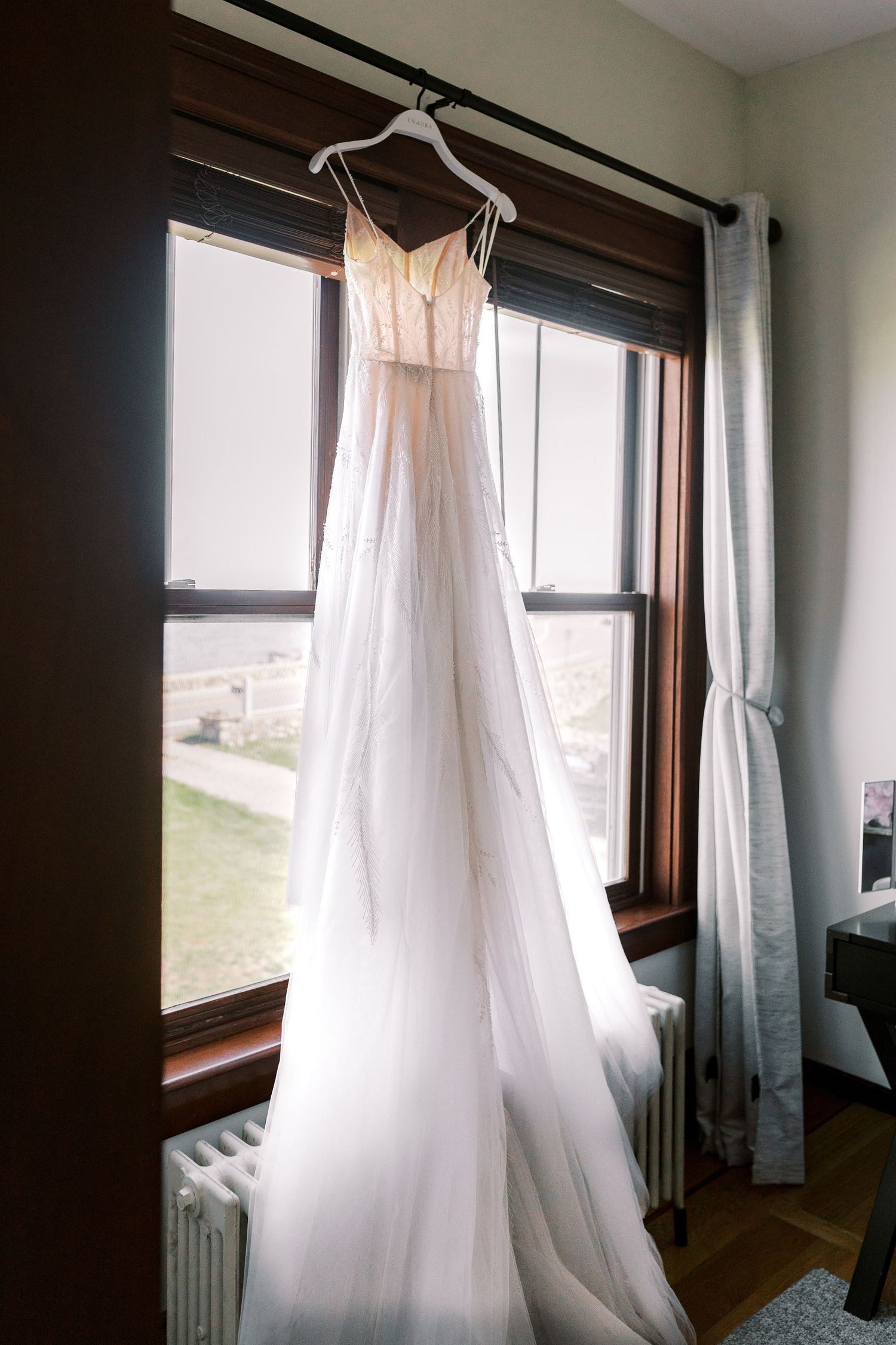 Ethereal white wedding dresses hanging by sunlit windows in a rustic room.
