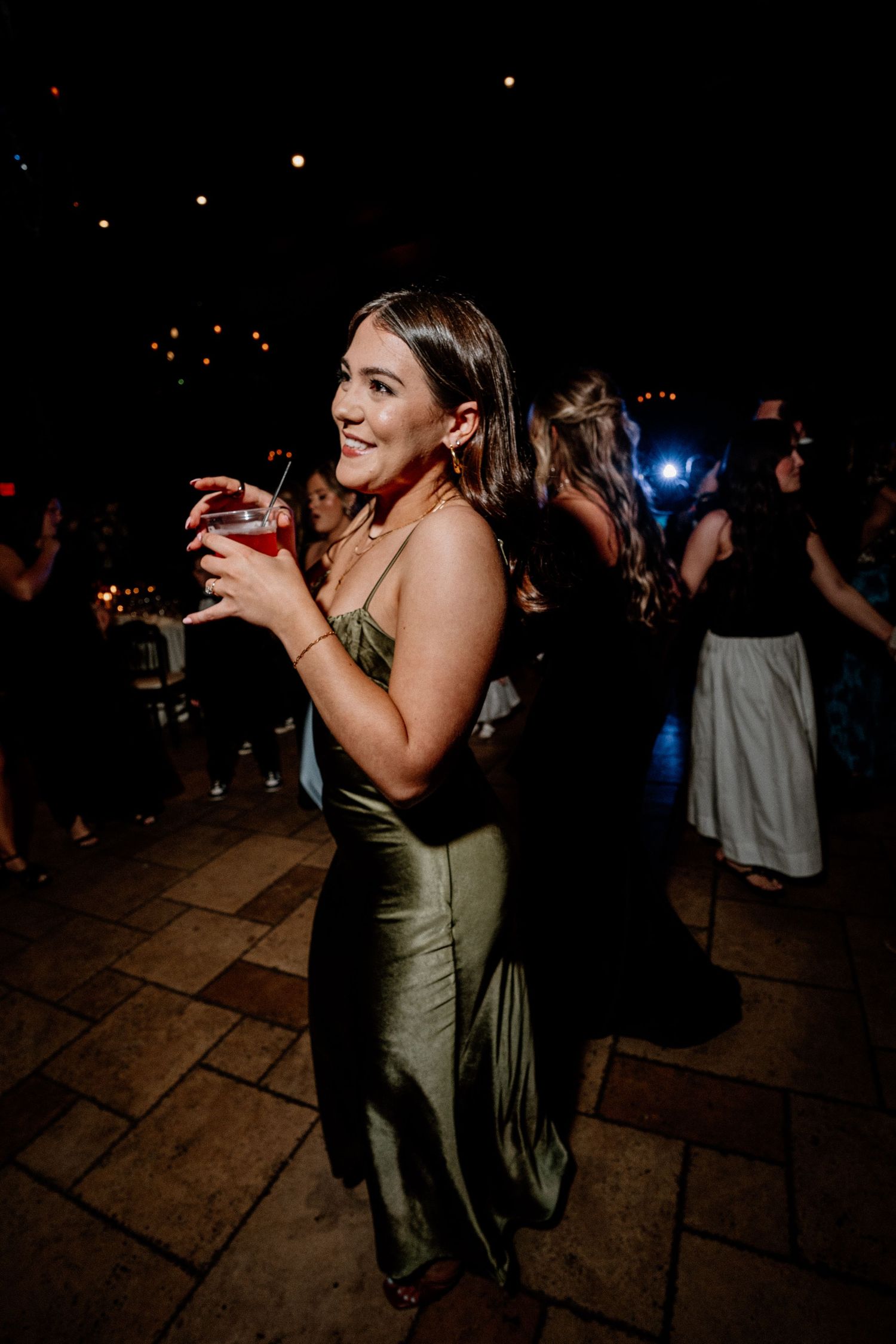 People dancing and celebrating at a dimly lit nighttime wedding reception on a stone patio.