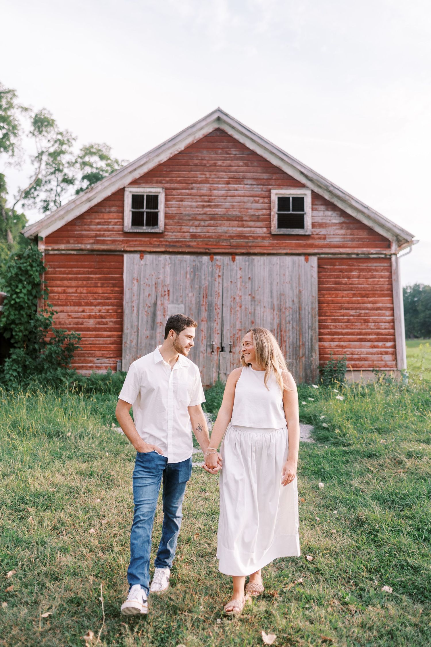A couple shares a tender moment near a red barn in a countryside setting.