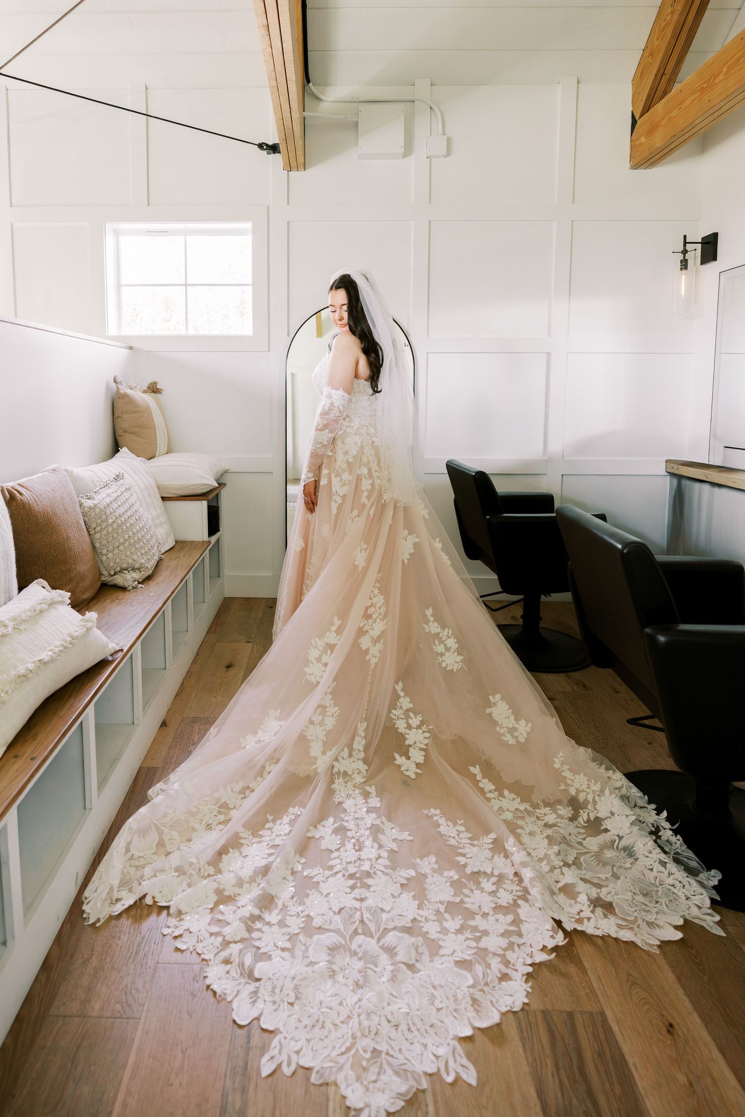 A stunning lace wedding gown with cathedral train displayed in a bright white room with hardwood floors.
