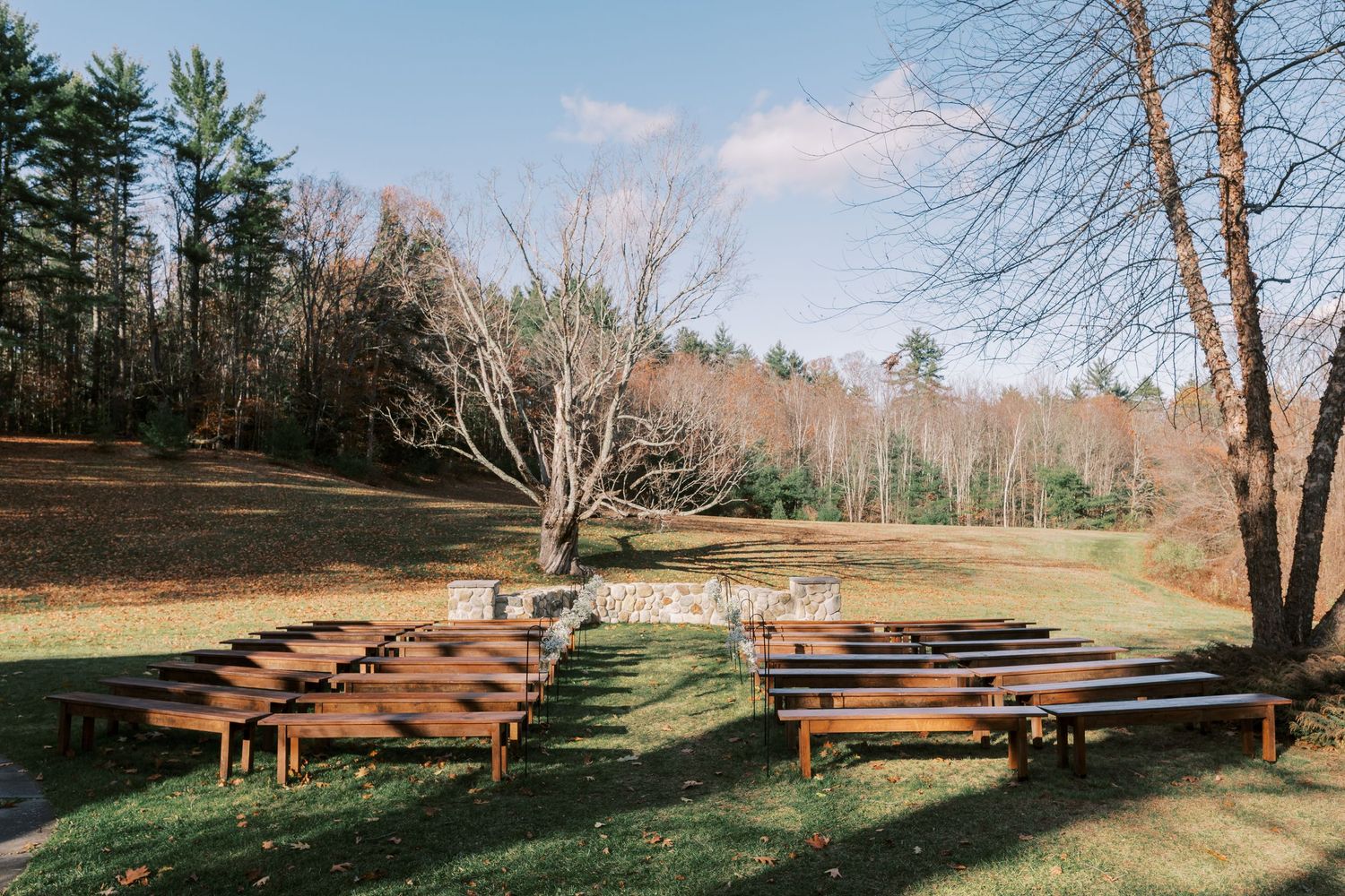 Wooden benches arranged in rows create an outdoor ceremony space surrounded by tall pine trees and natural landscaping.