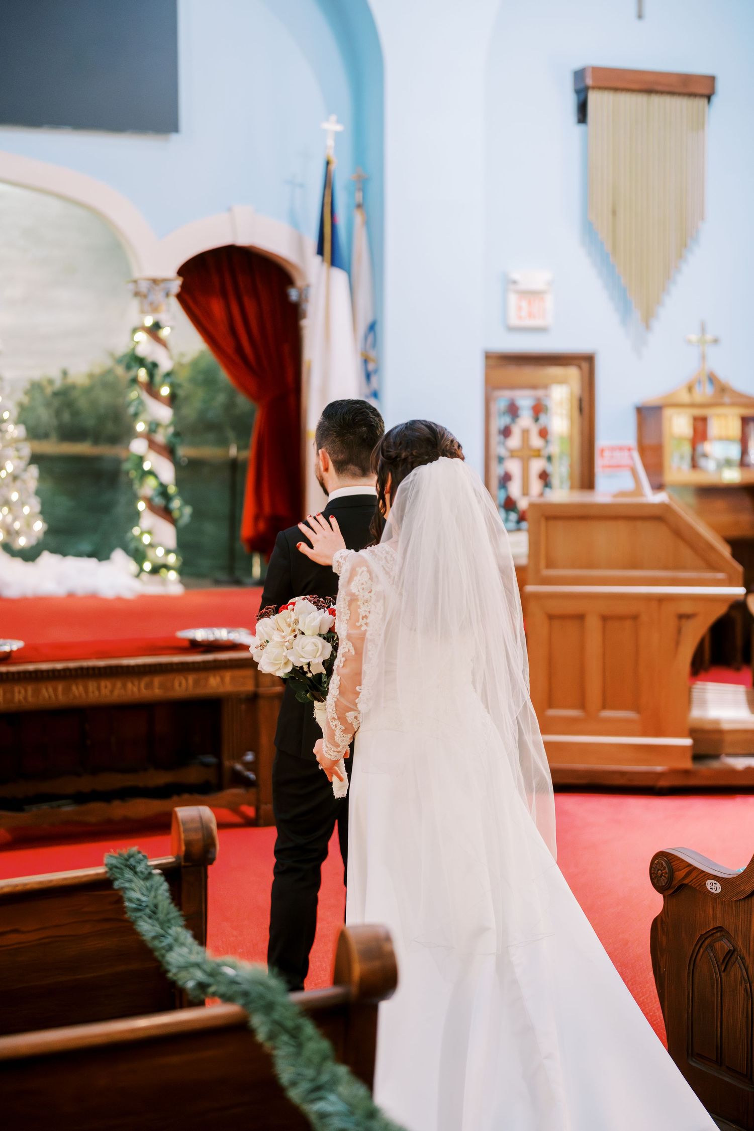 A couple stands at the altar in a church with blue walls and floral decorations.