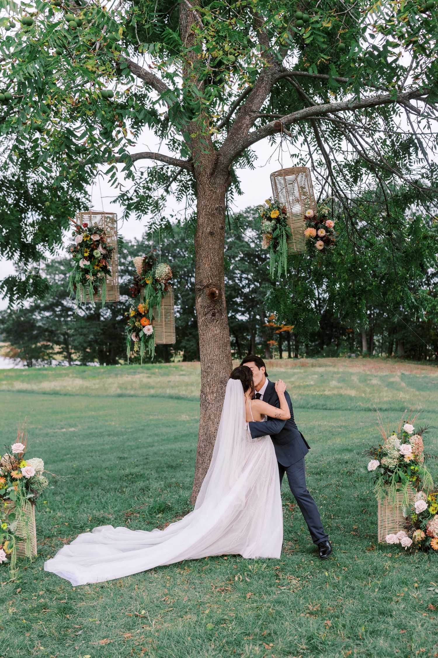 Romantic outdoor wedding photoshoot under a tree decorated with hanging lanterns and floral arrangements.