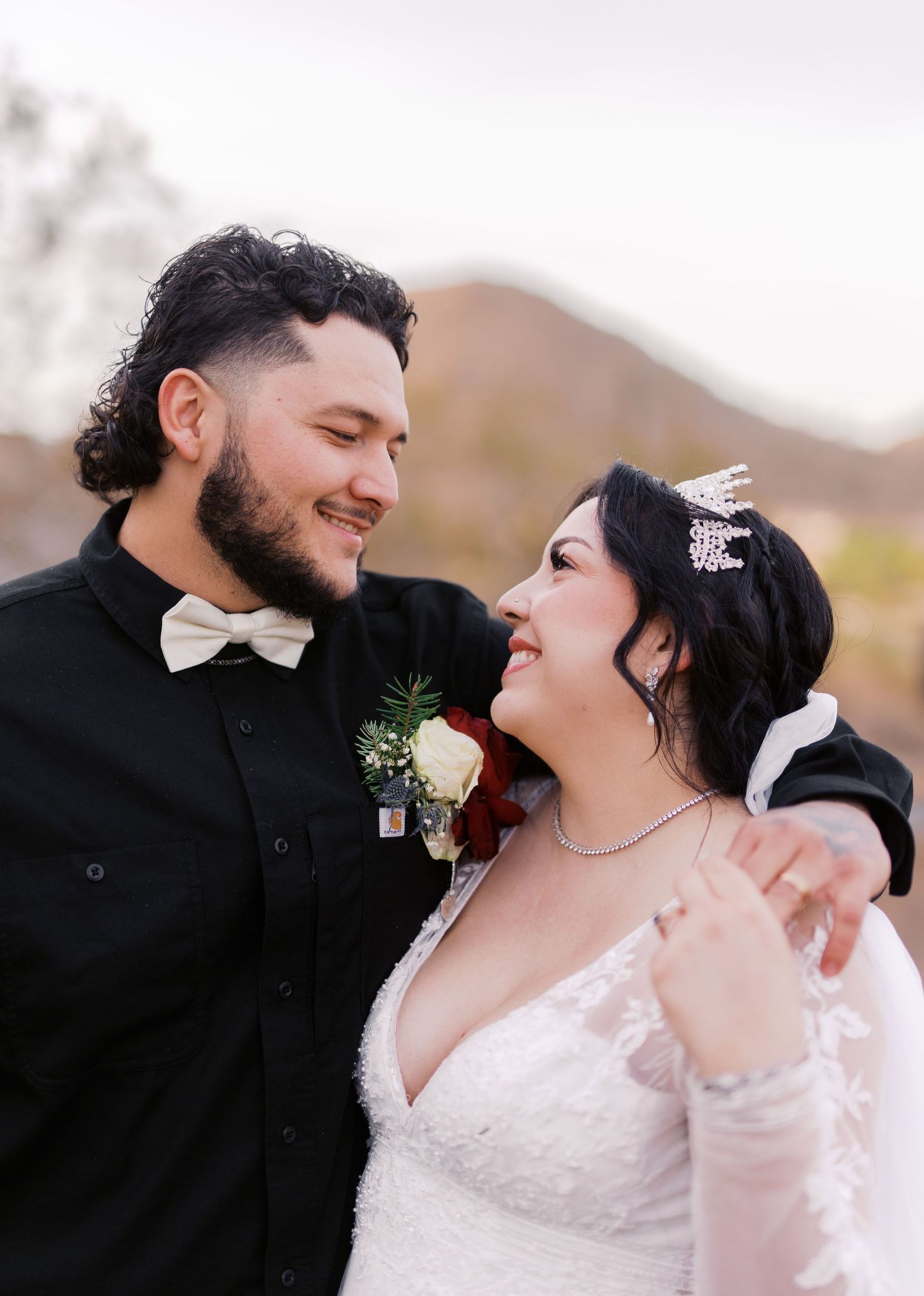A joyful wedding couple sharing an intimate moment outdoors with mountains visible in the background.