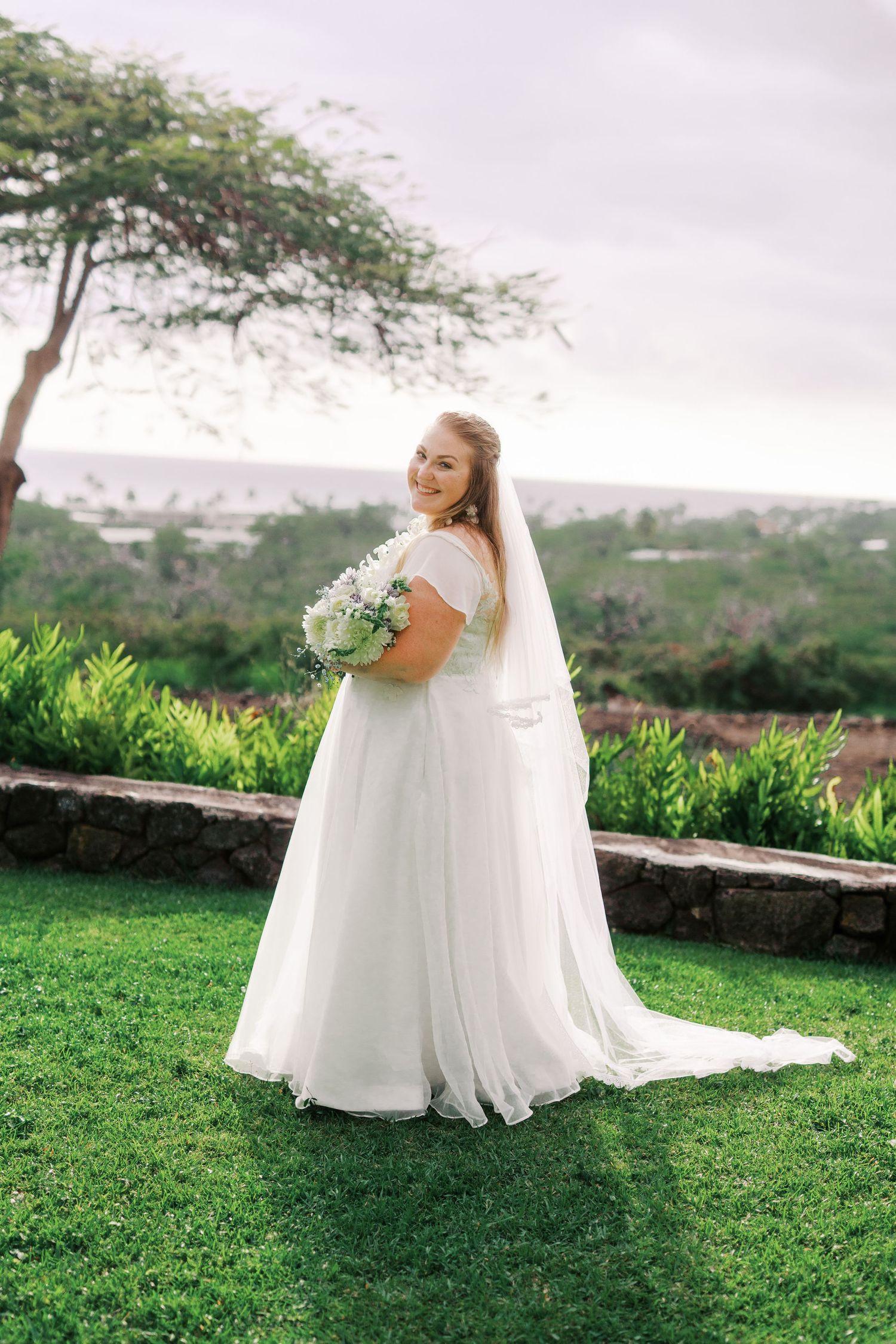 Ethereal bridal portraits of someone in a flowing white gown against a scenic green landscape.