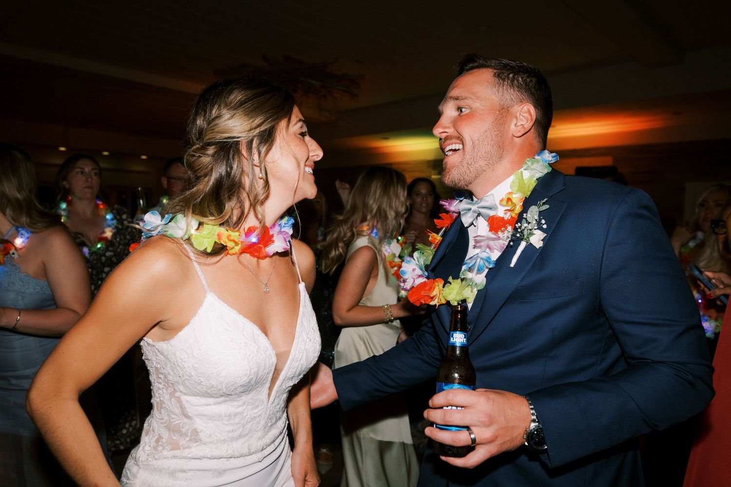 A couple dances together at a wedding reception with colorful lighting and floral decorations in the background.
