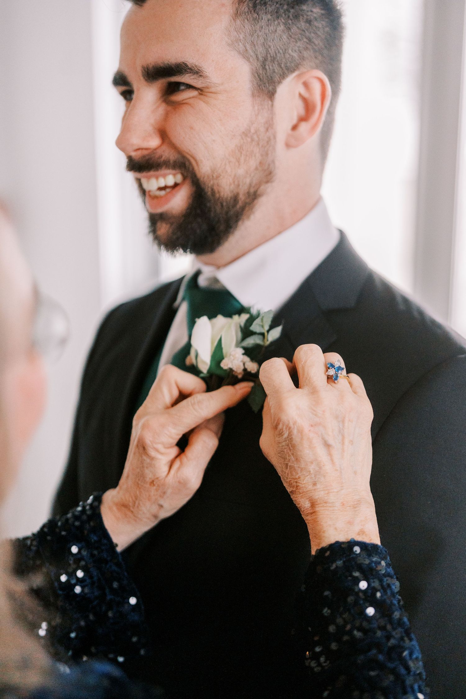 Hands adjusting a white boutonniere on a black suit jacket during wedding preparations.