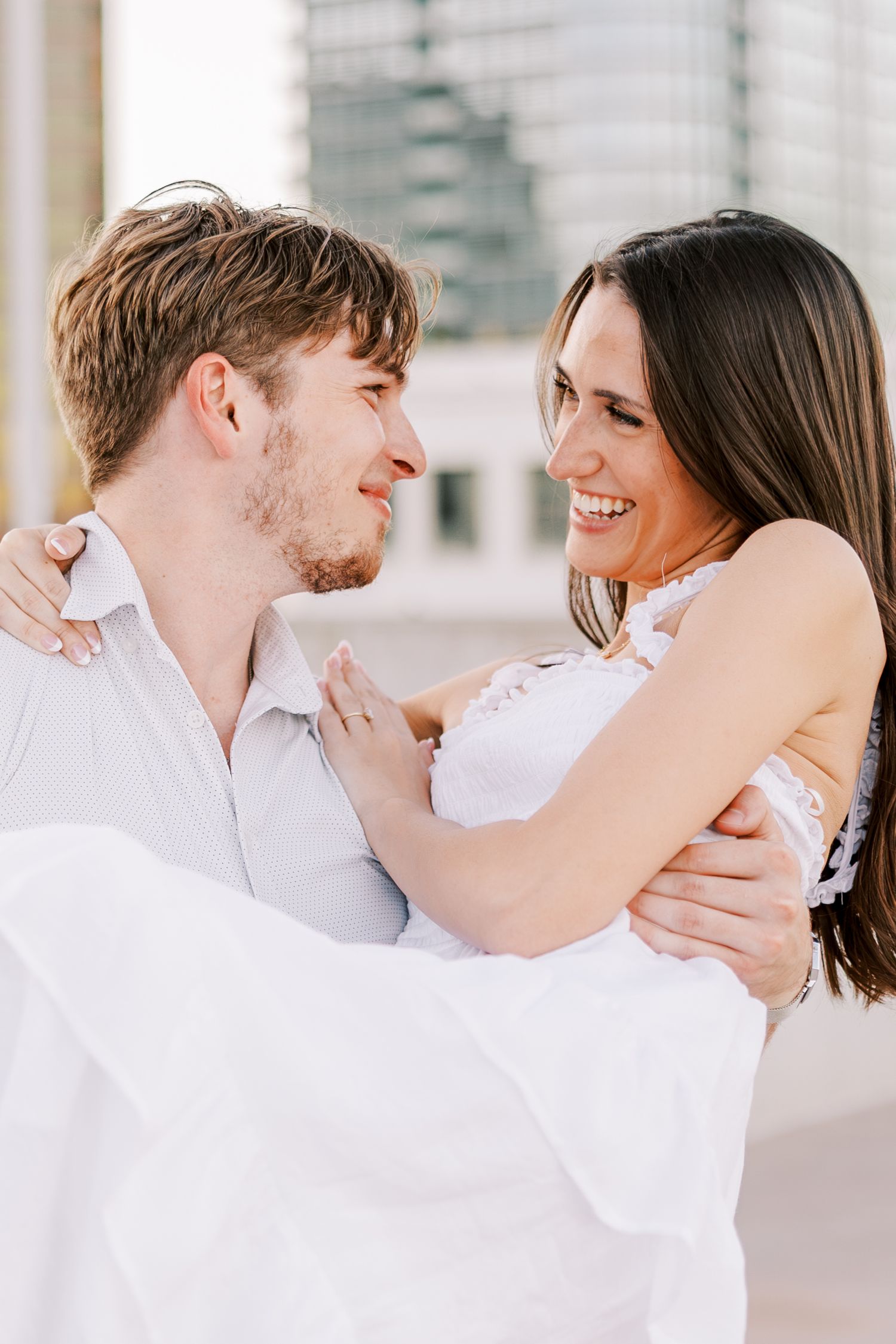 Couple in white sharing intimate moments during rooftop photoshoot with urban backdrop.
