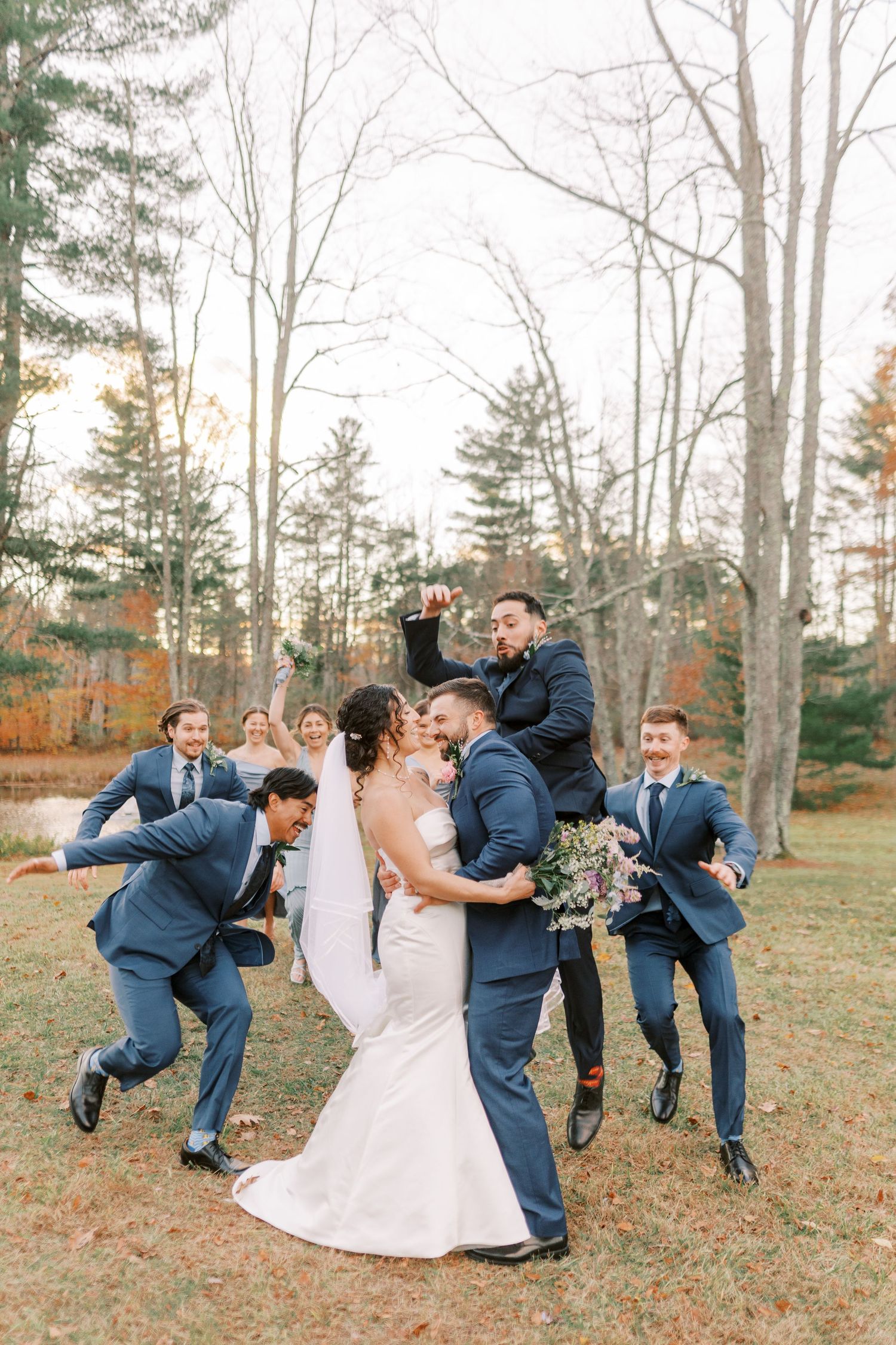 Wedding party in navy suits and white dress perform fun falling domino effect pose sequence in autumn forest setting.