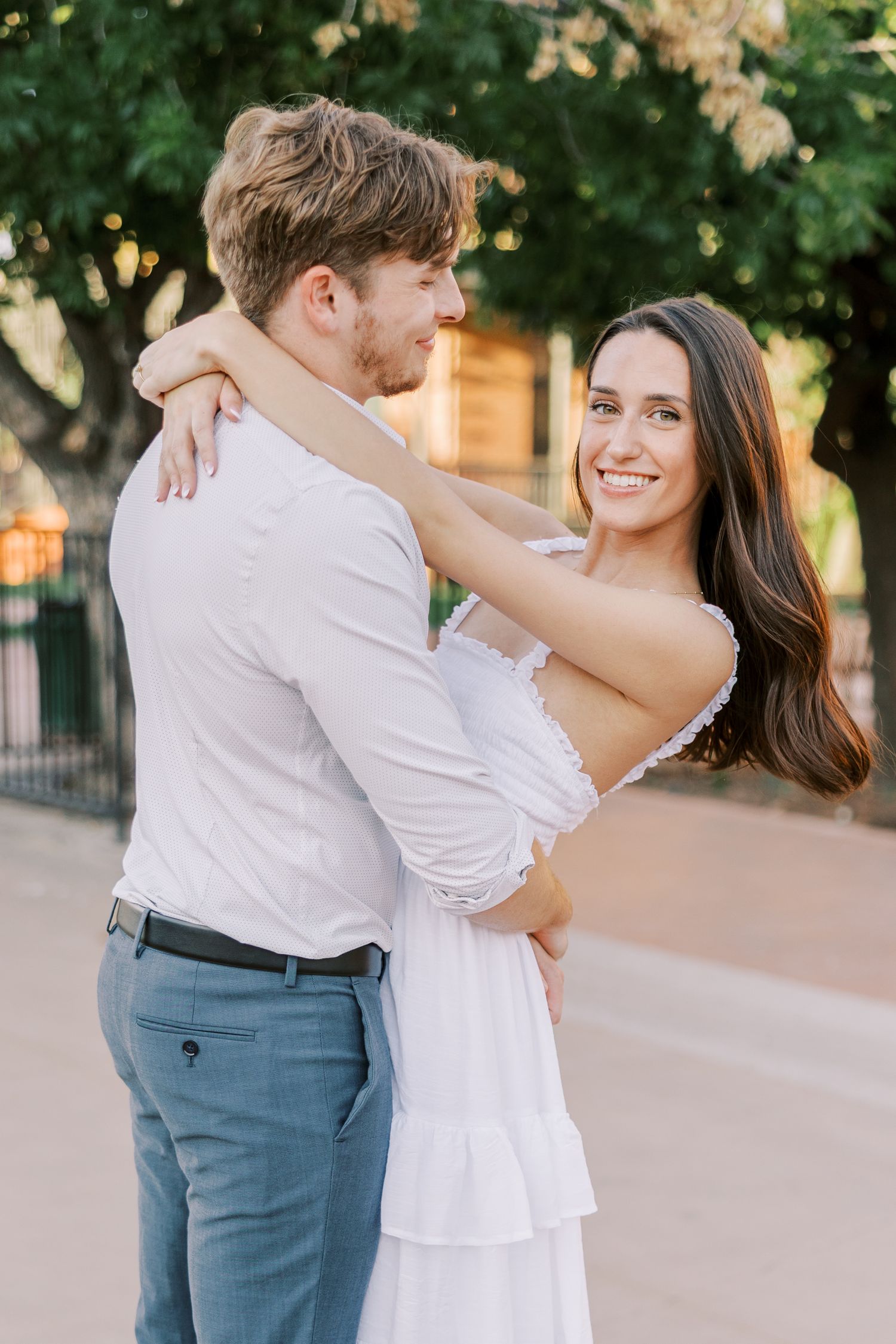 A couple in white and blue attire embraces romantically in an outdoor setting during a photo session.