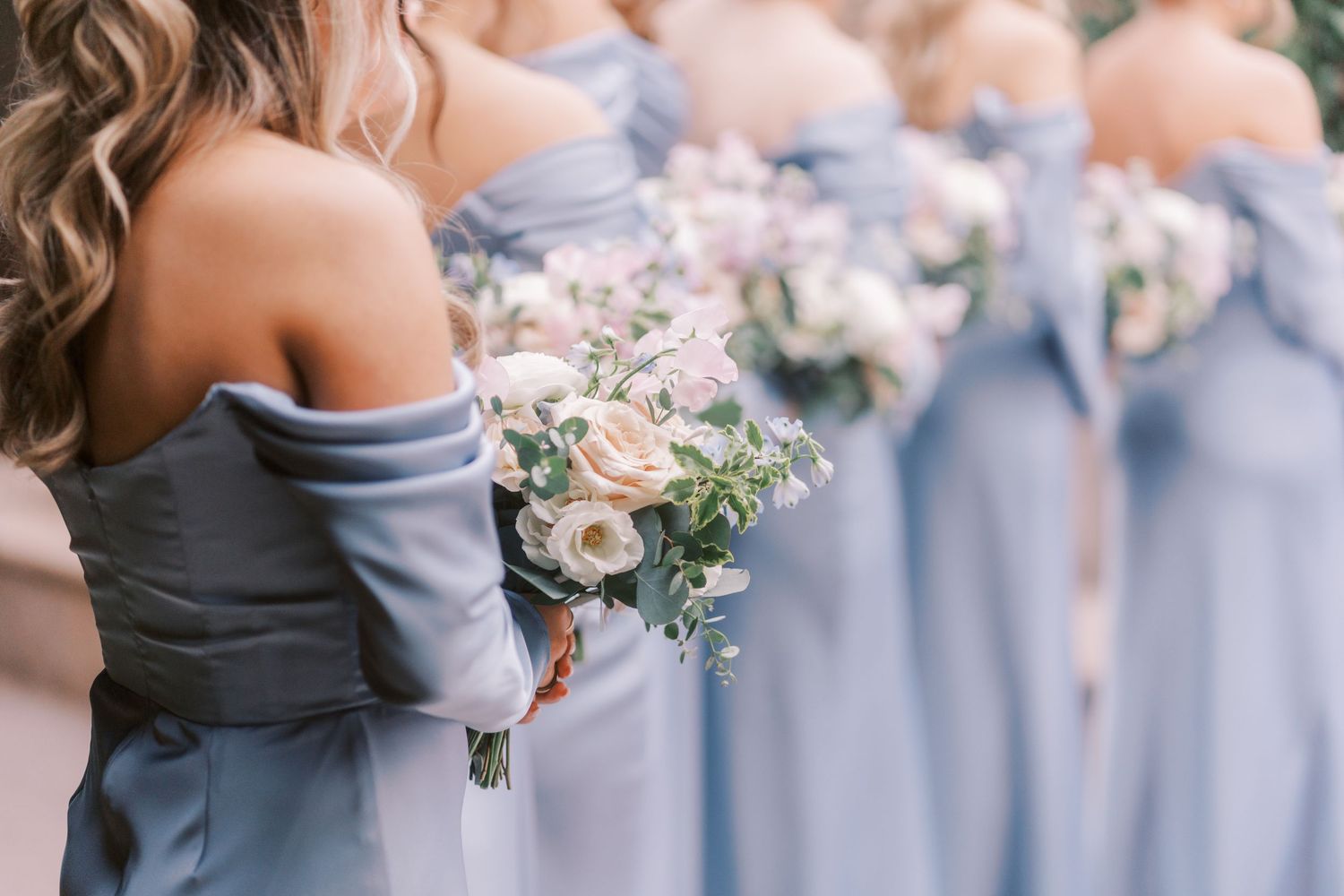 Wedding party members in coordinating blue and gray dresses pose together while holding floral bouquets.