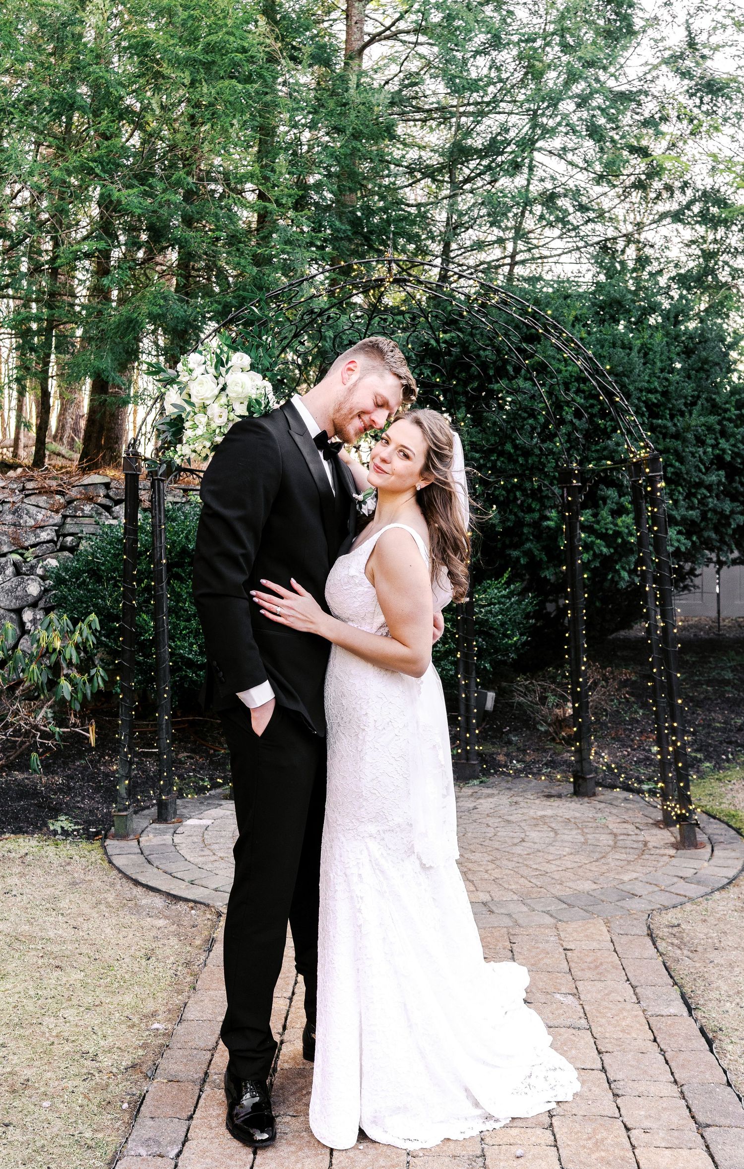 Newlyweds share an intimate moment on a brick patio surrounded by greenery.