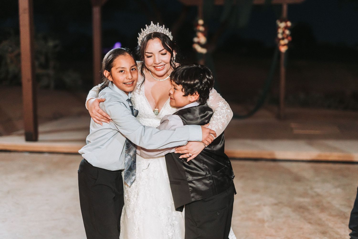 A heartwarming moment at a wedding as two young guests embrace the bride on the dance floor.