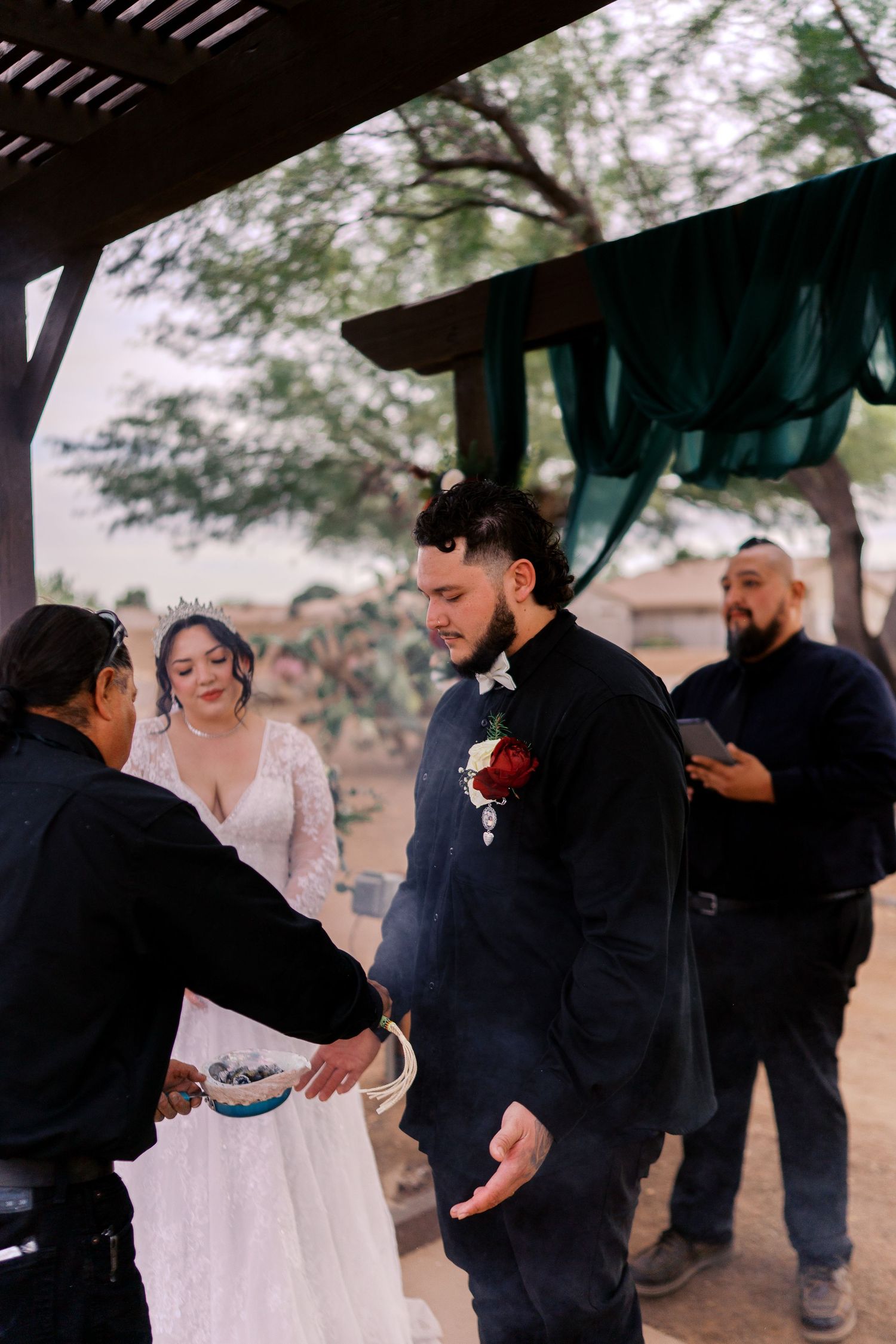 An outdoor wedding ceremony with guests gathered under a covered patio area at dusk.