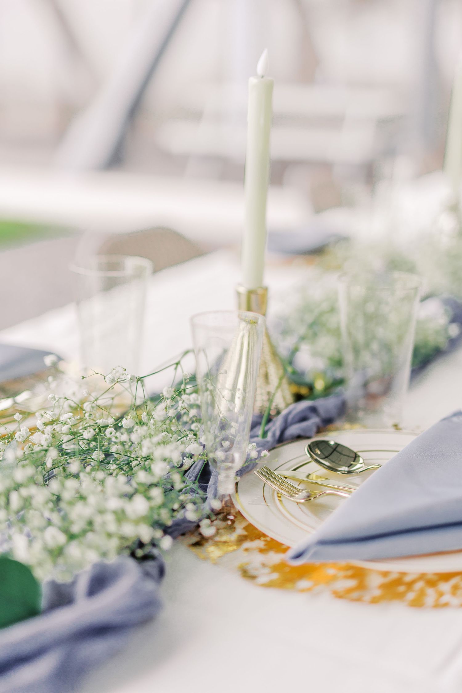 Elegant wedding table setting with white candles, delicate flowers, and blue napkins.