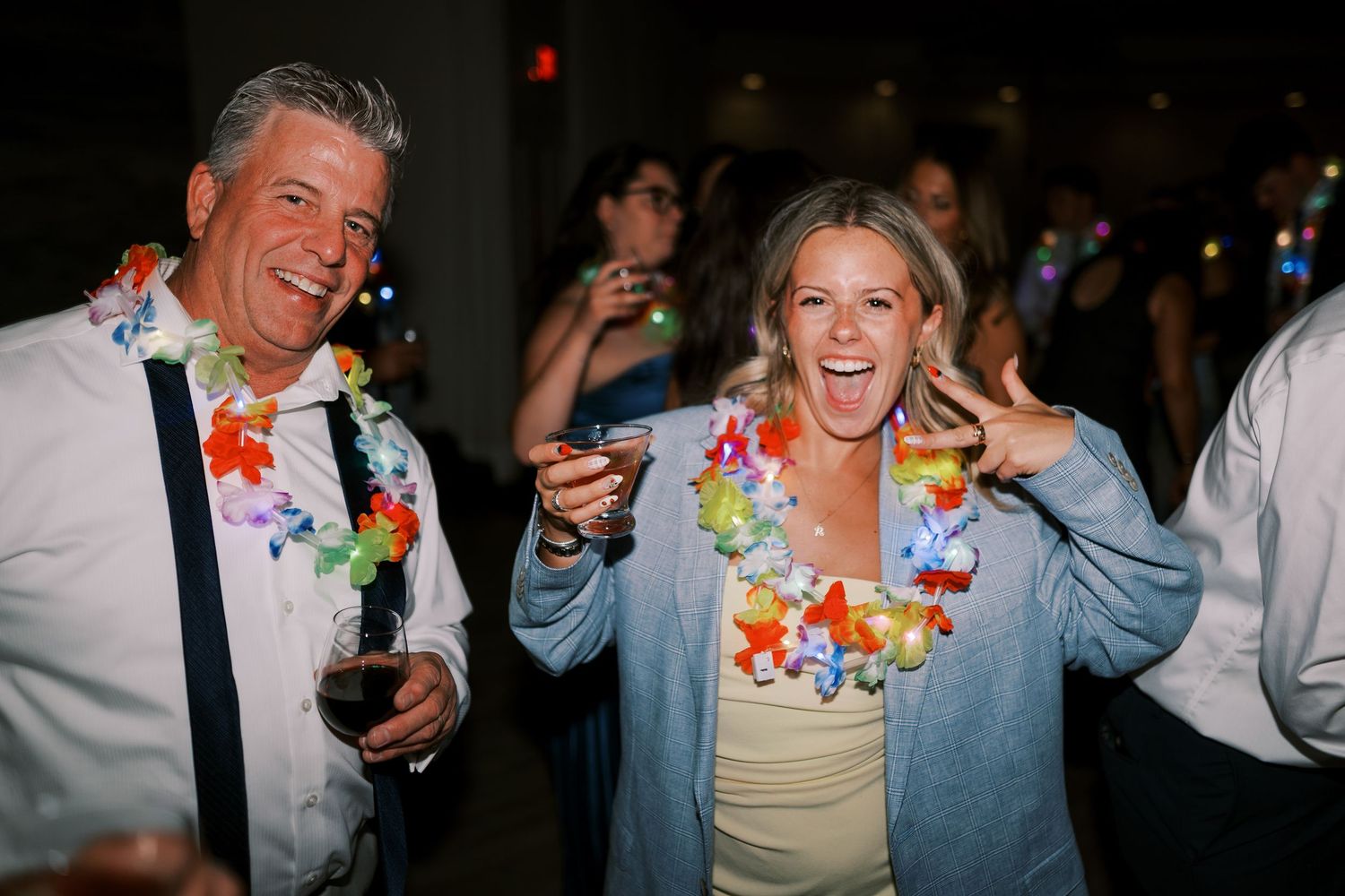 People wearing colorful leis celebrate at a party with drinks and laughter.