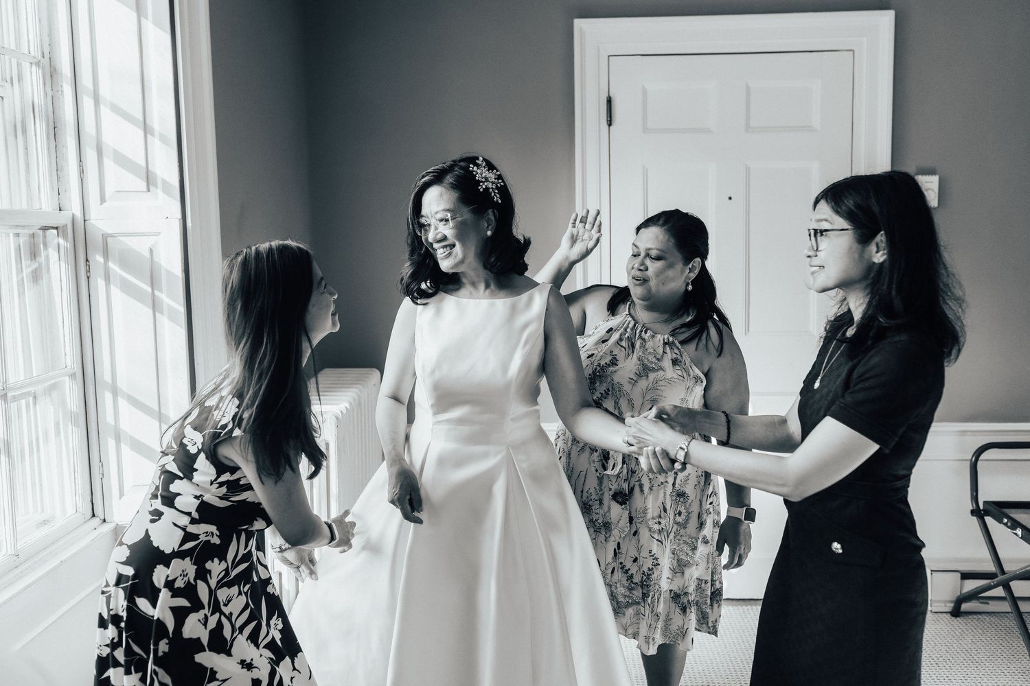 Wedding party getting ready indoors with bridesmaids assisting and sharing joyful moments together.