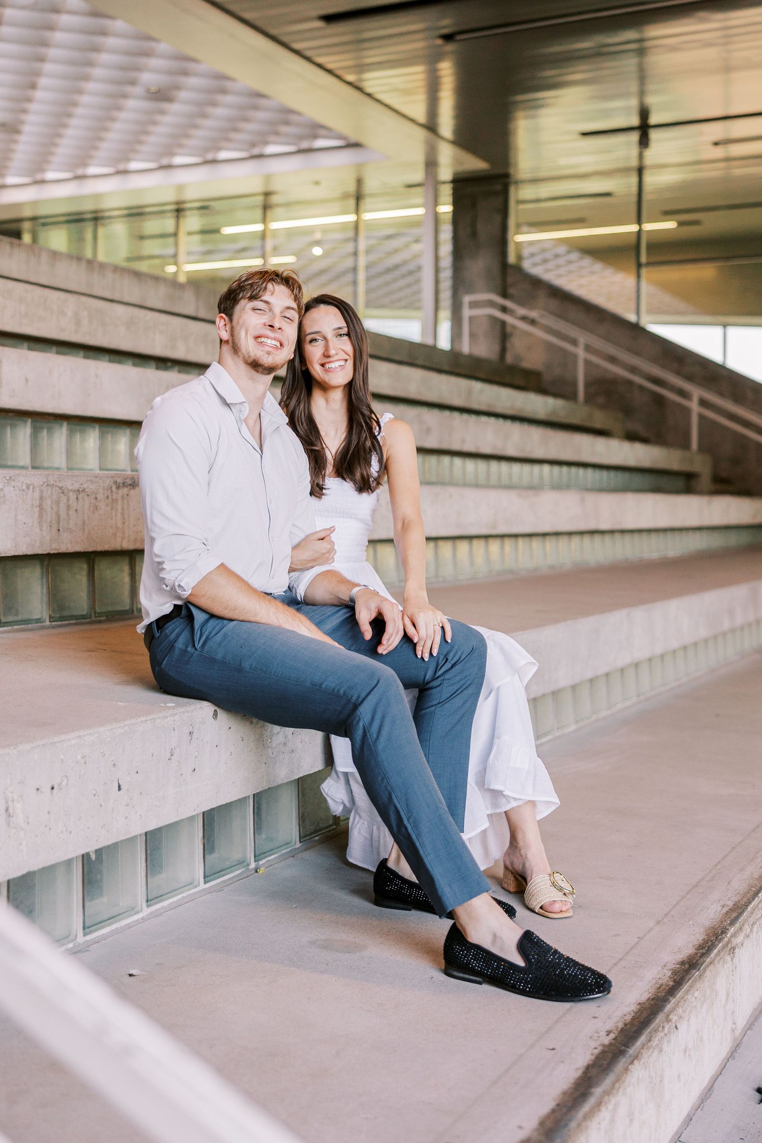 A couple sits together on concrete steps in a modern building with a casual romantic mood.