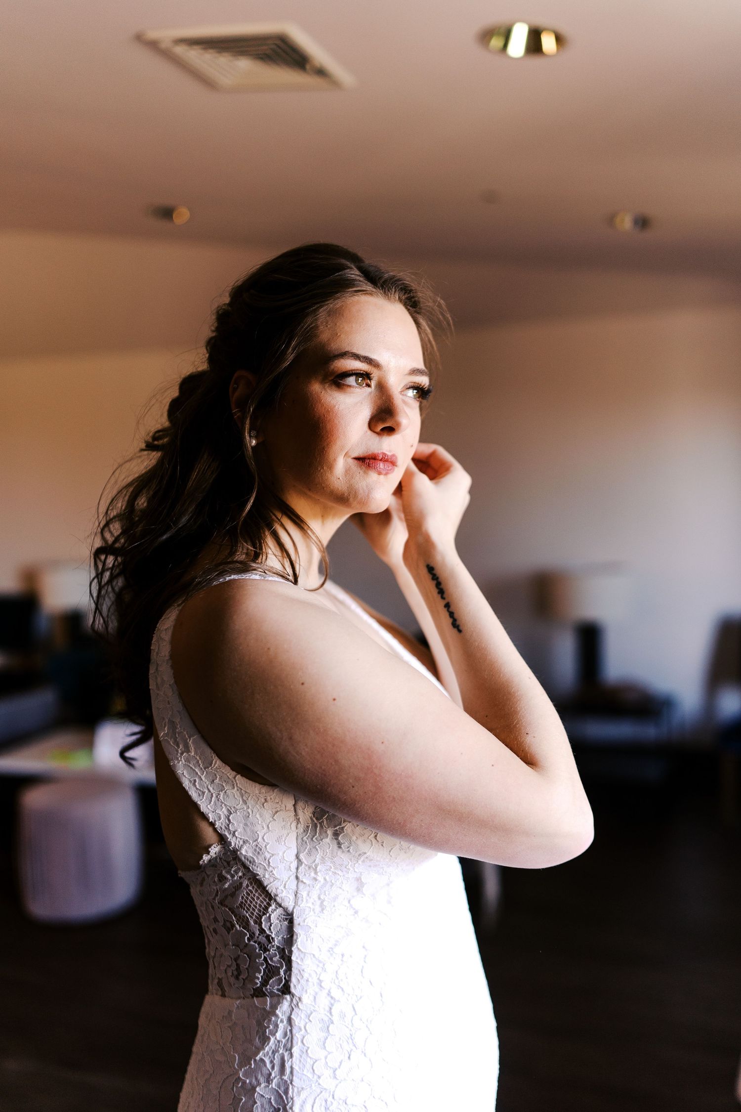 Bride in lace wedding dress adjusting earrings while getting ready.