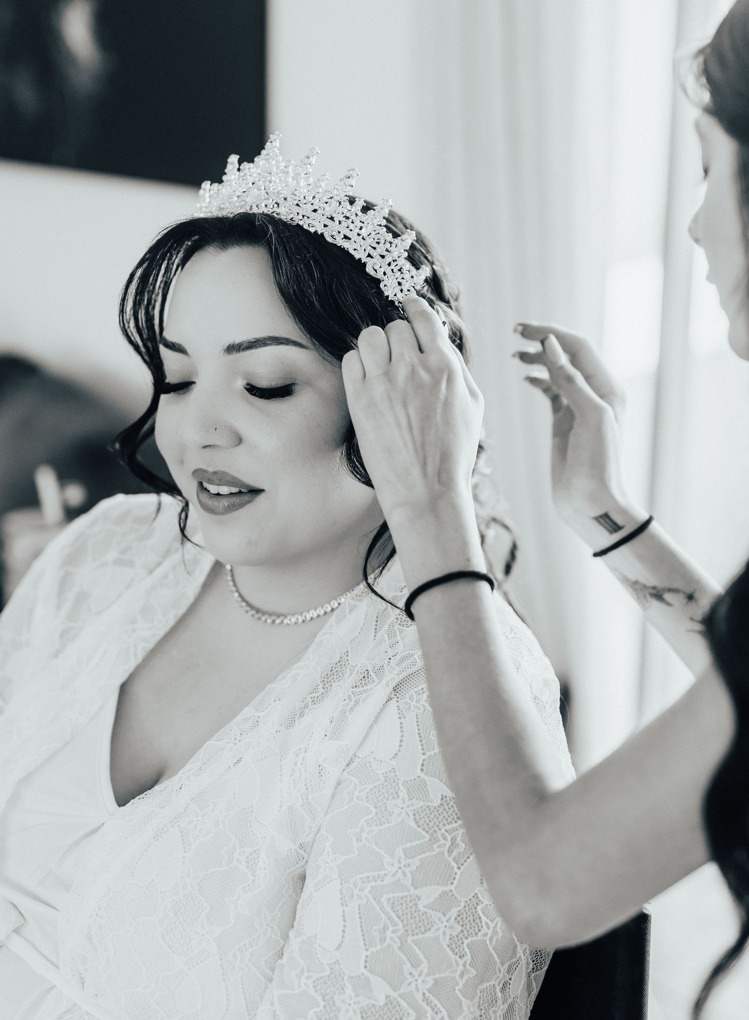 Black and white photo of bride wearing sparkly tiara and lace dress during wedding preparation.