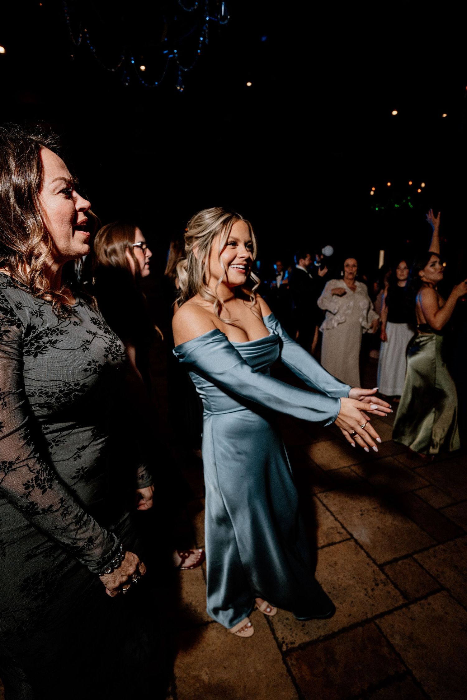 Guests dancing energetically at a dimly lit wedding reception on a dance floor.