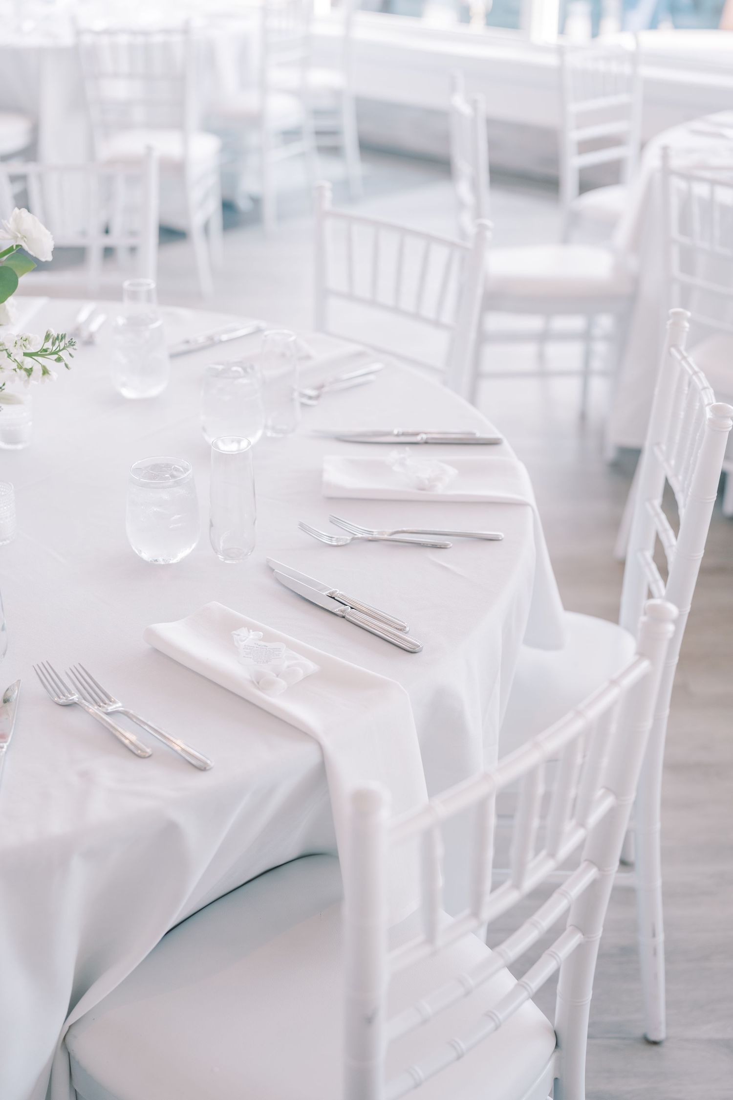 Elegant white wedding reception tables with crisp linens and place settings arranged in a bright, airy venue.