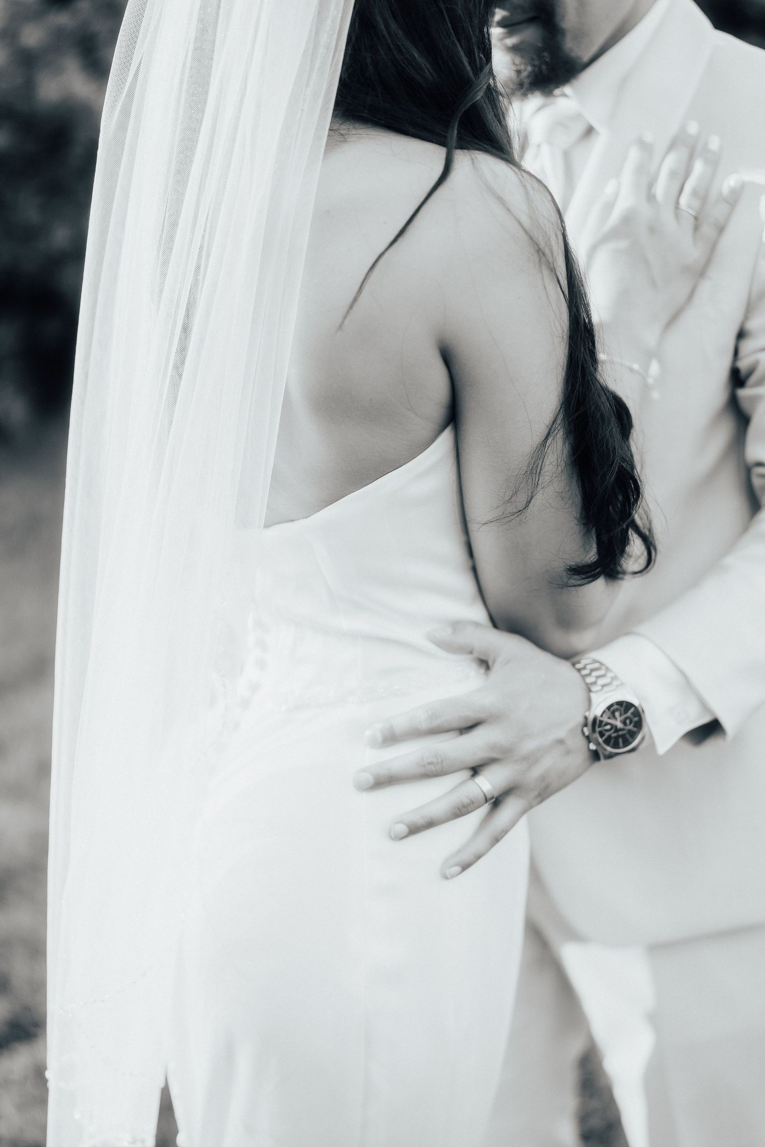 A black and white wedding photo showing an intimate embrace between a couple in elegant white attire.