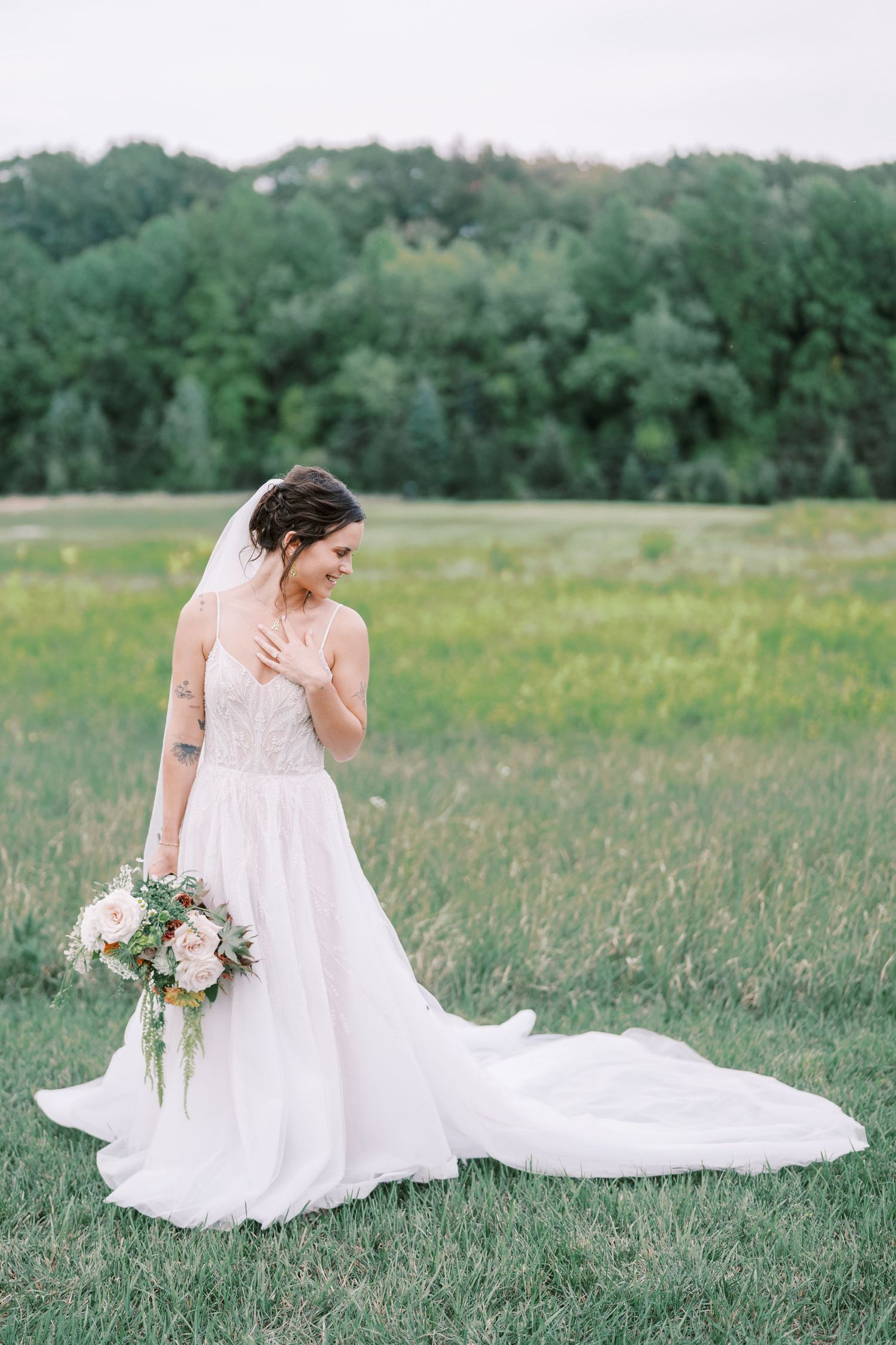 Bride in flowing white gown poses gracefully in meadow with trailing train.