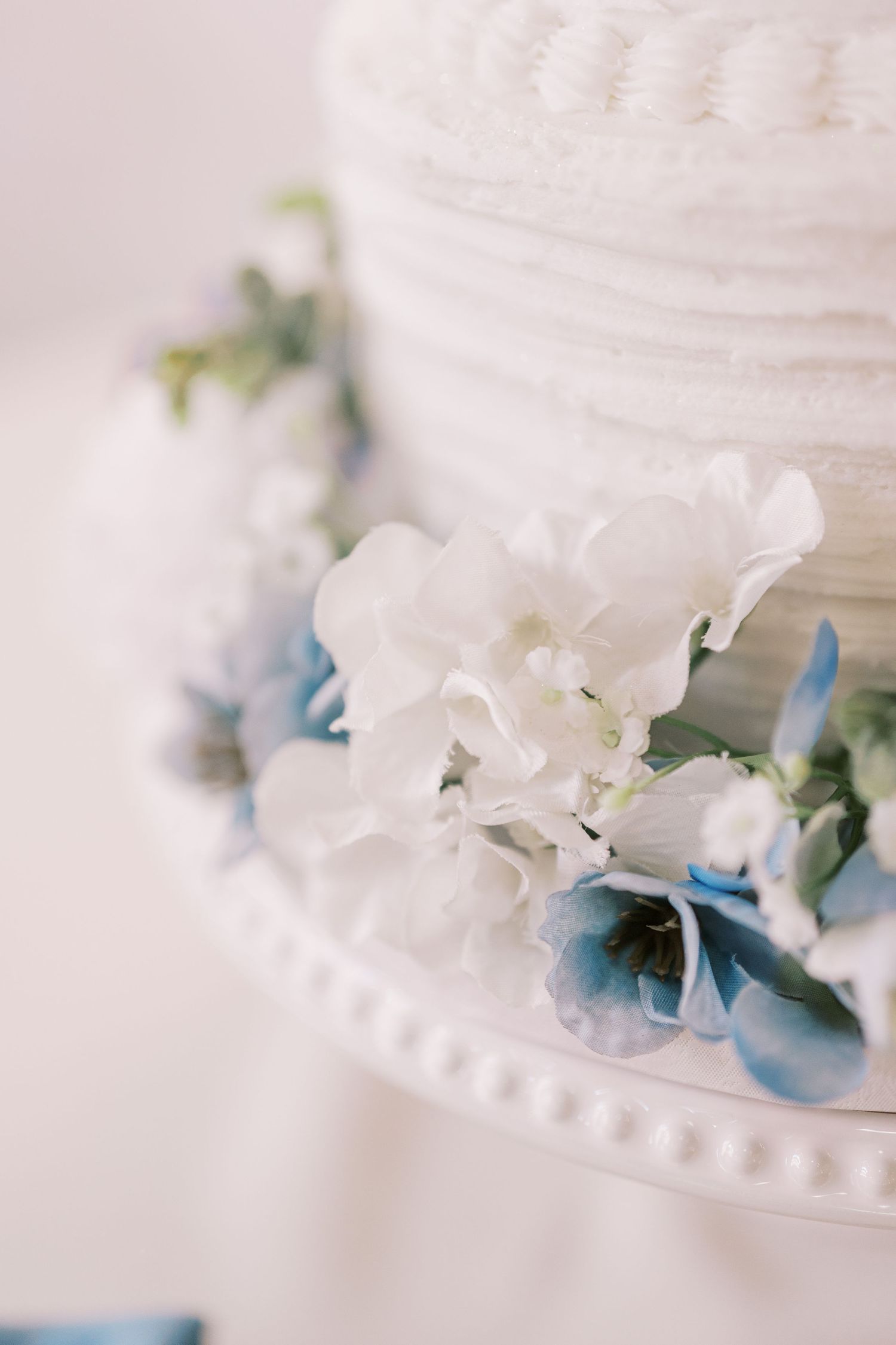Close-up details of a white wedding cake decorated with delicate blue hydrangea flowers and white floral accents.