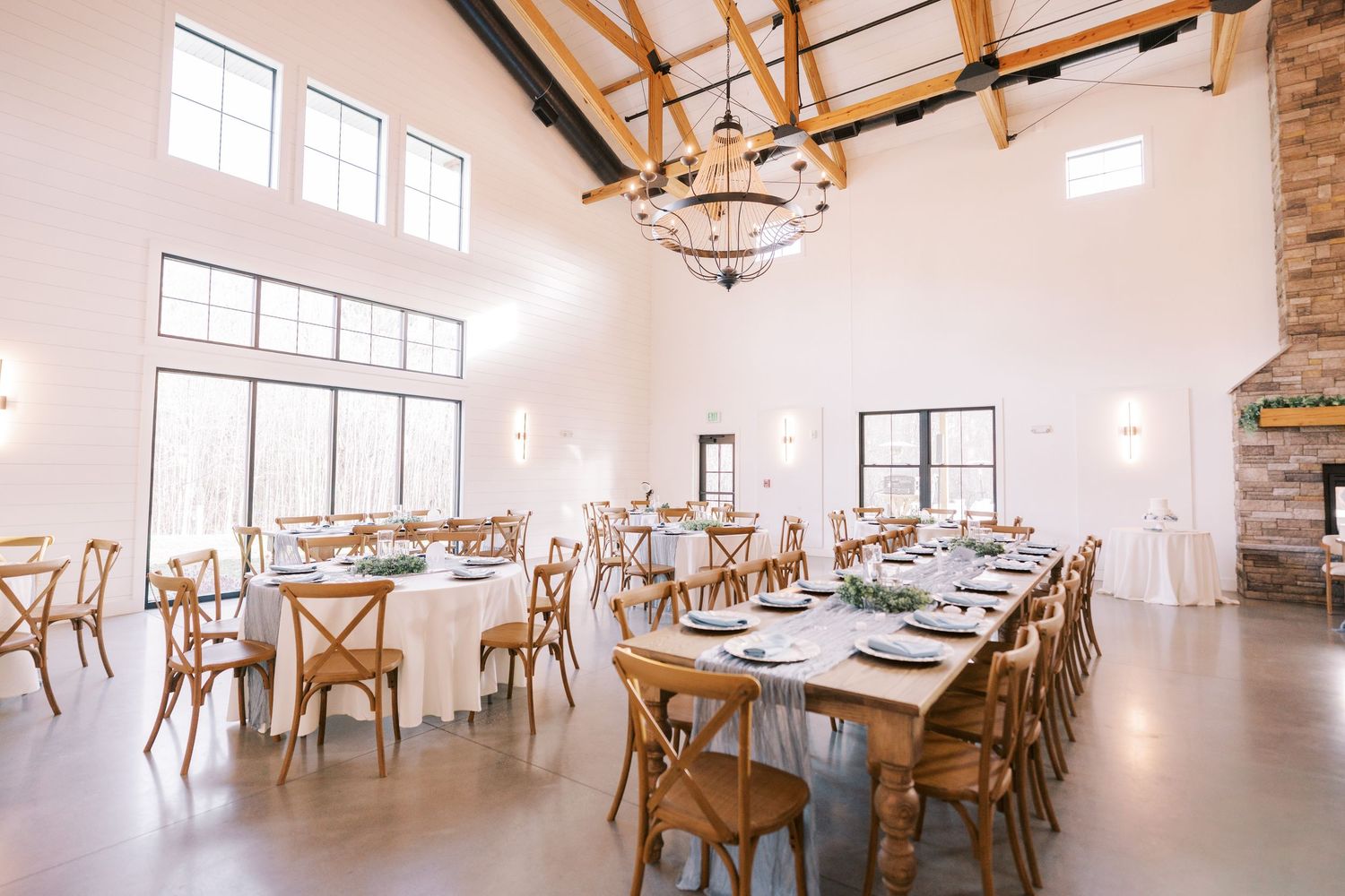 Modern rustic event venue with exposed wood beams, white walls, and elegant table settings in a bright open space.
