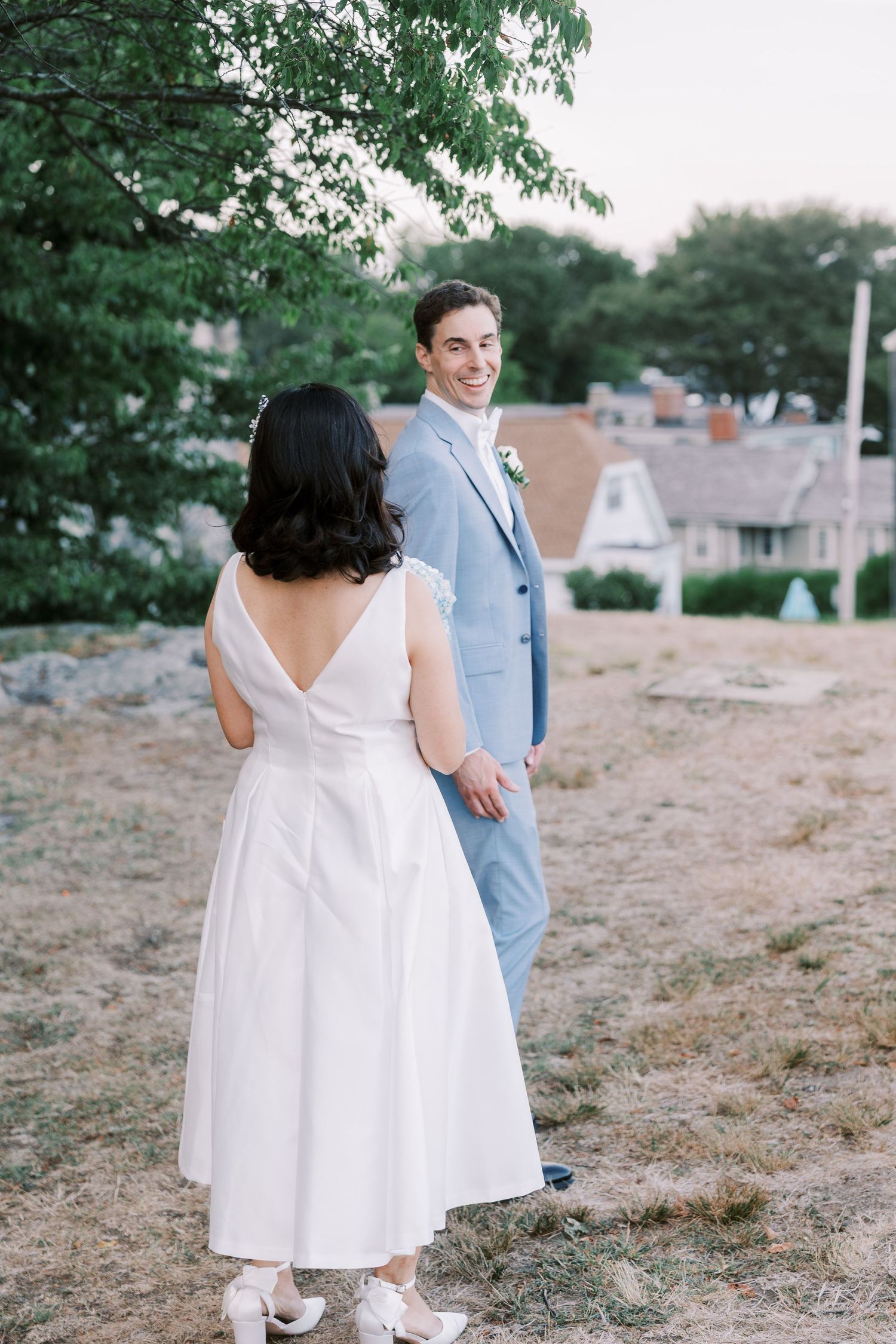 A couple takes wedding photos in a natural seaside setting with grass and trees.