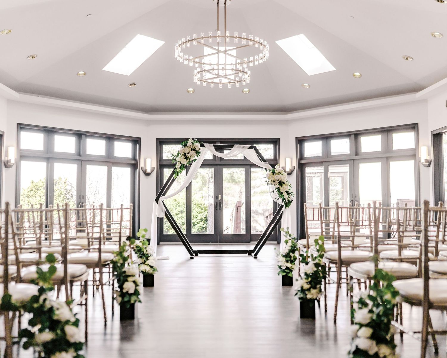 A bright, modern event venue with floor-to-ceiling windows, chandeliers, and elegant floral arrangements throughout the space.
