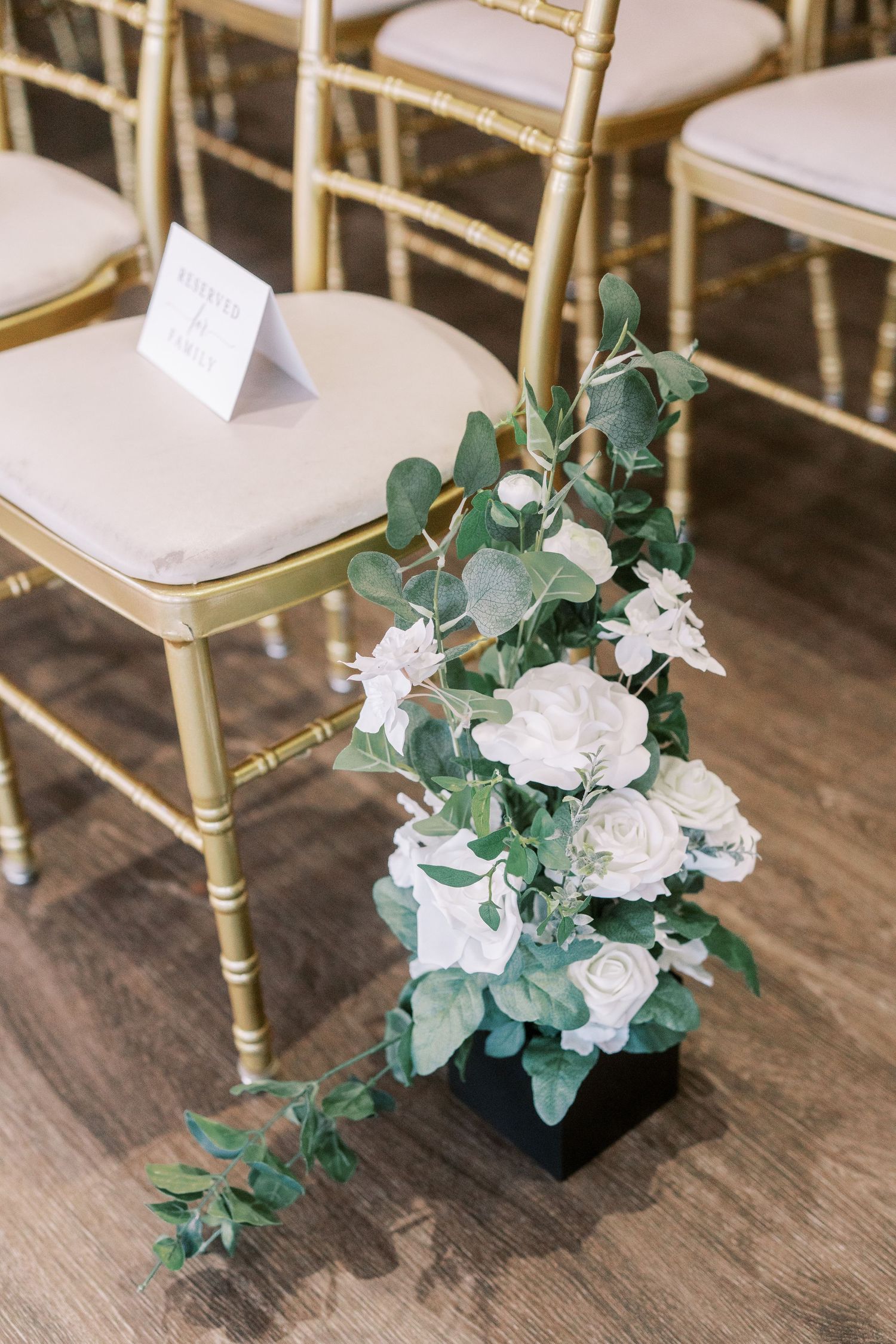 Gold Chiavari chairs decorated with white roses and eucalyptus for a wedding ceremony.