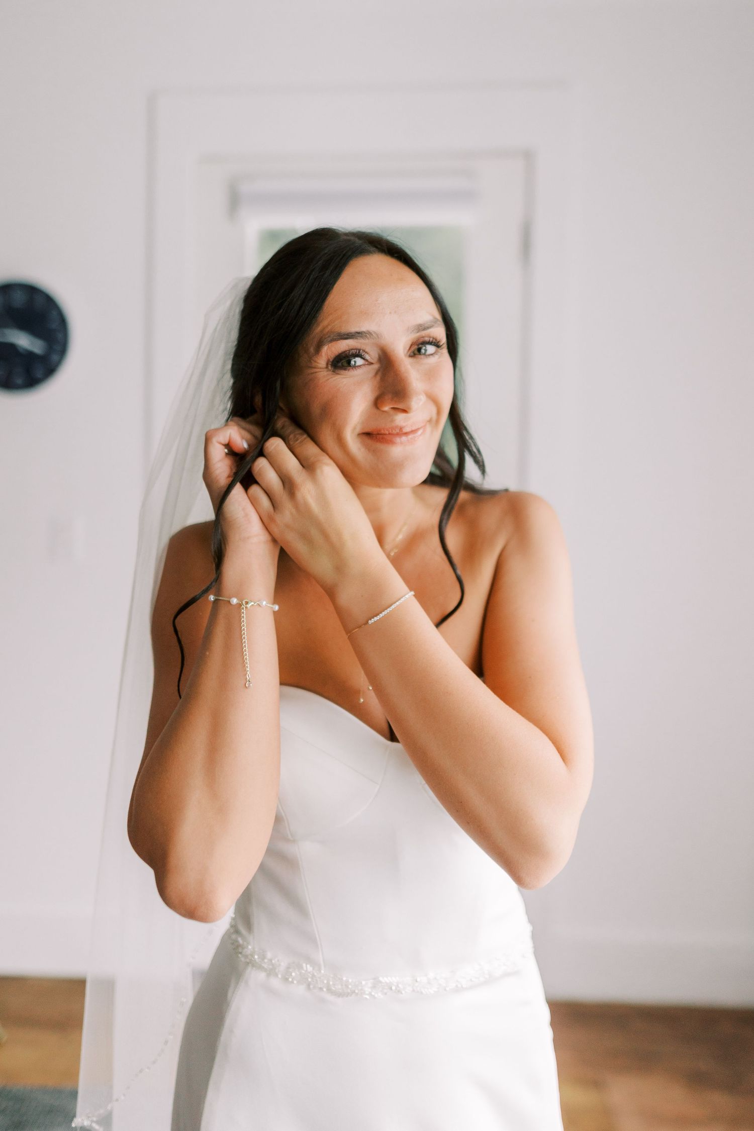 Bride in white wedding dress adjusting earrings during getting ready preparations.