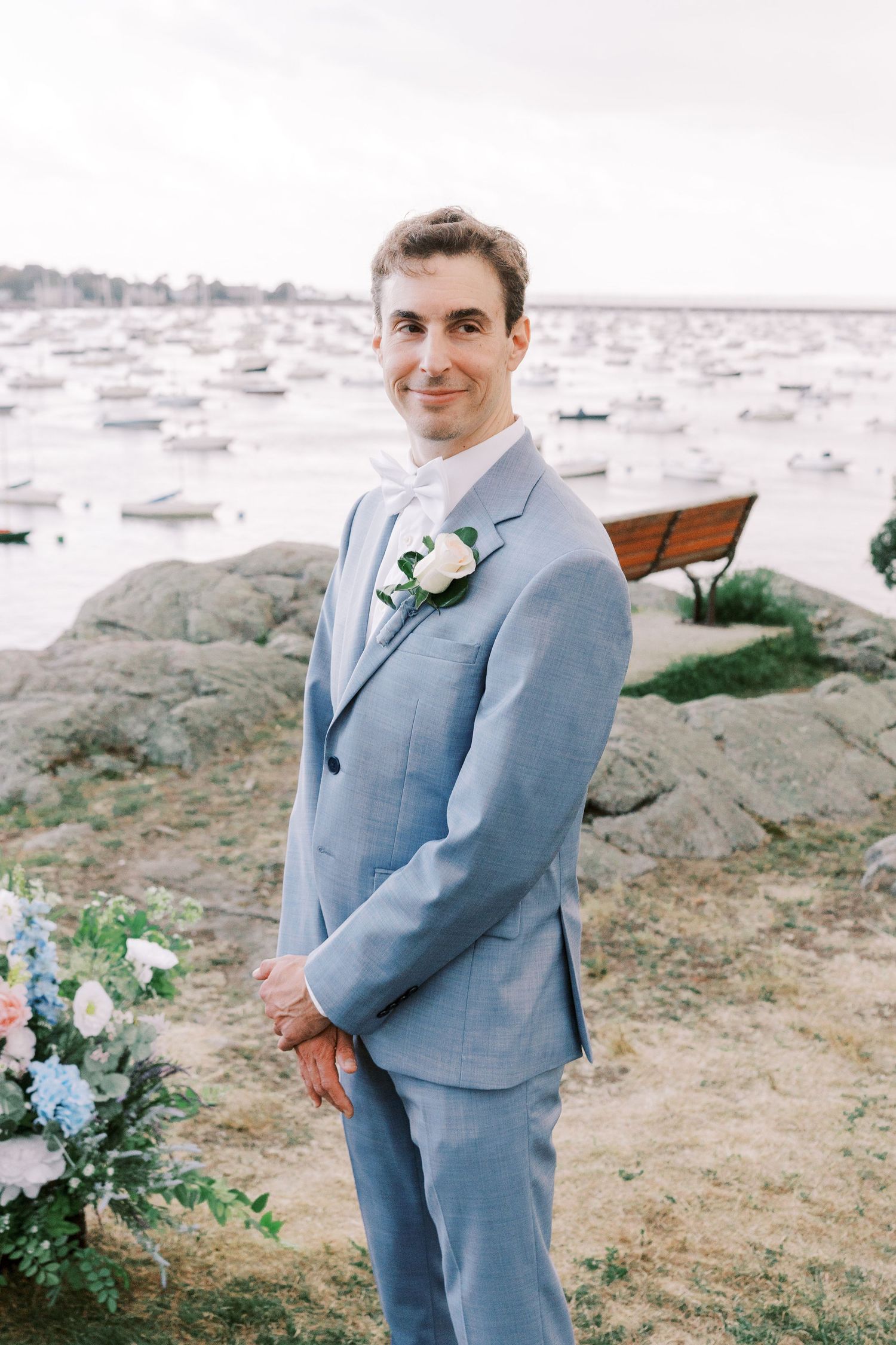 A wedding portrait session on rocky coastal terrain with boats and water in the background.