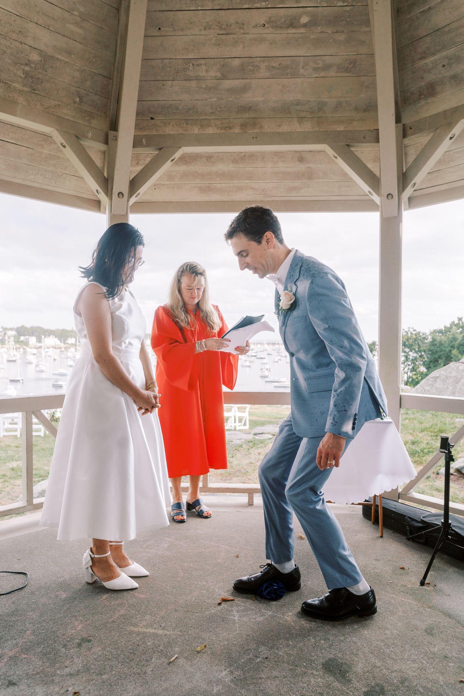 Wedding party members prepare under a wooden gazebo shelter.