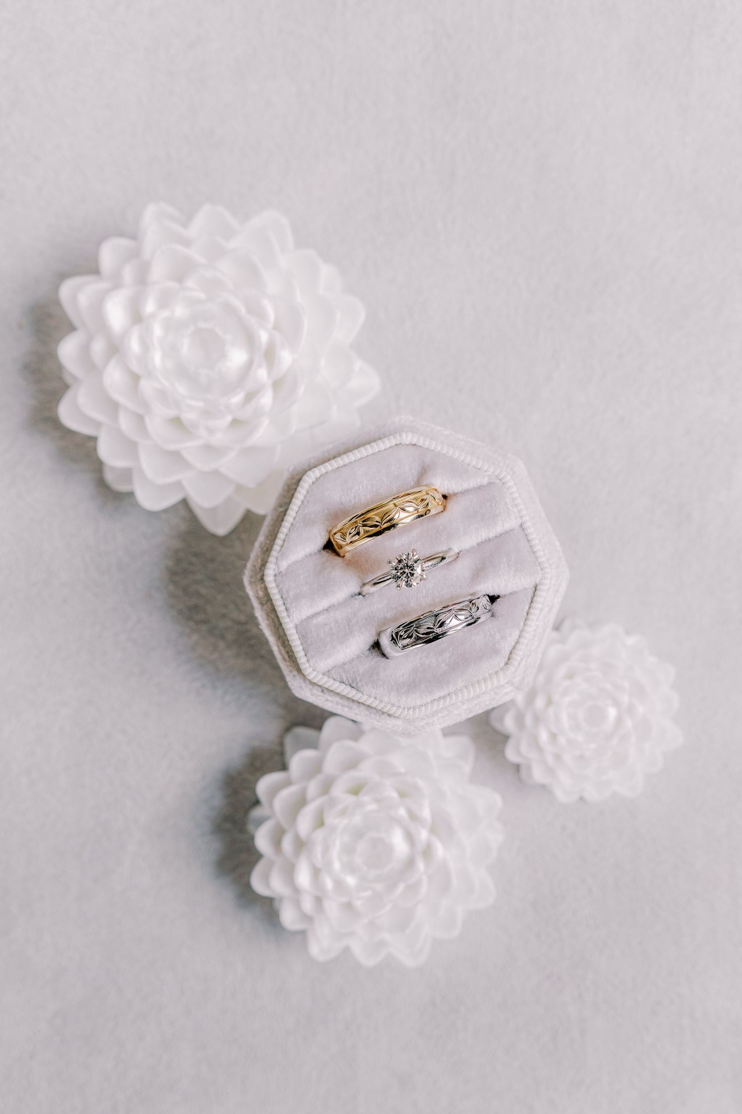 Wedding rings nestled in velvet hexagonal ring box surrounded by delicate white floral decorations.