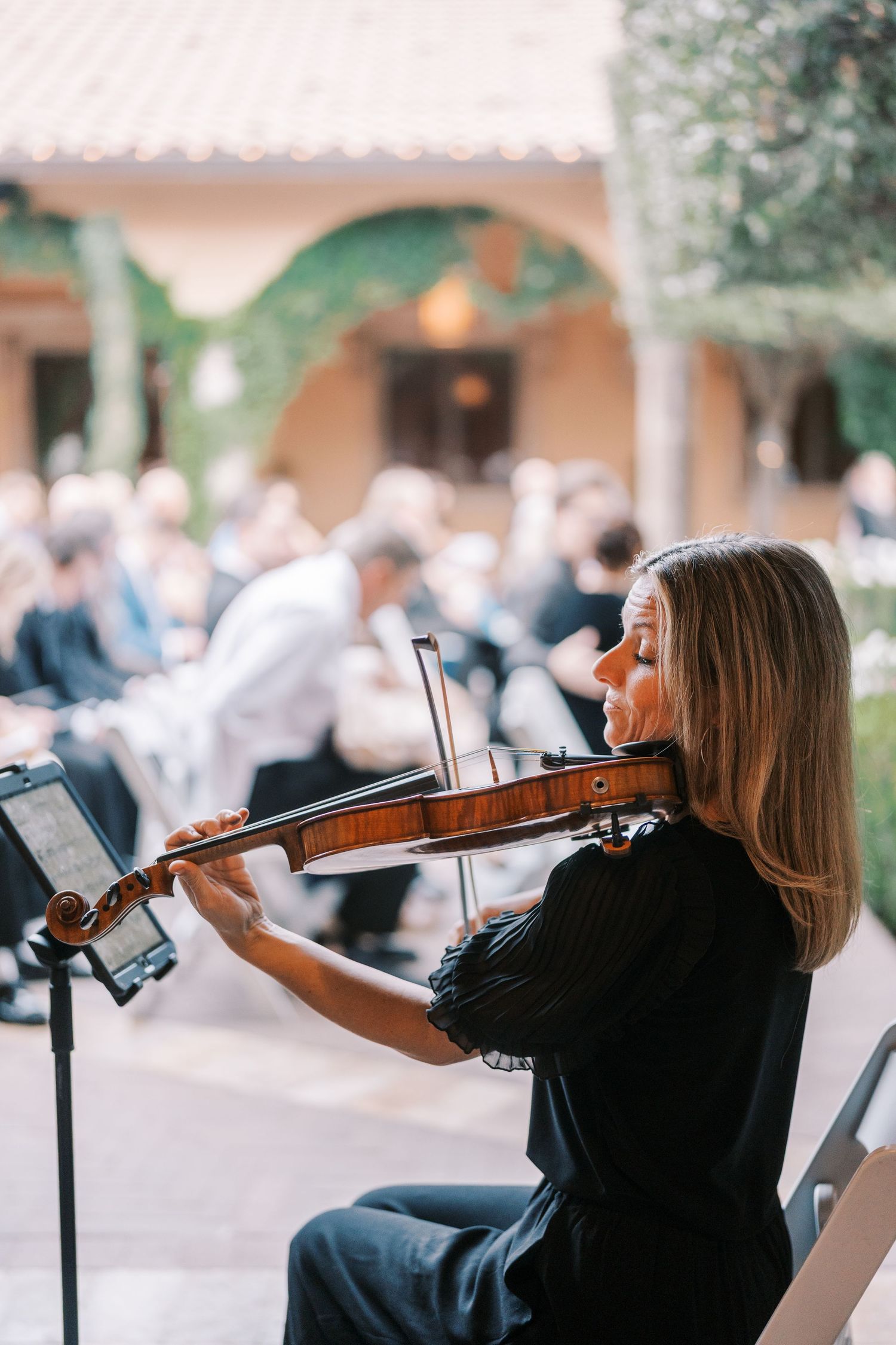 A violinist performs outdoors at an event venue with blurred audience members in the background.