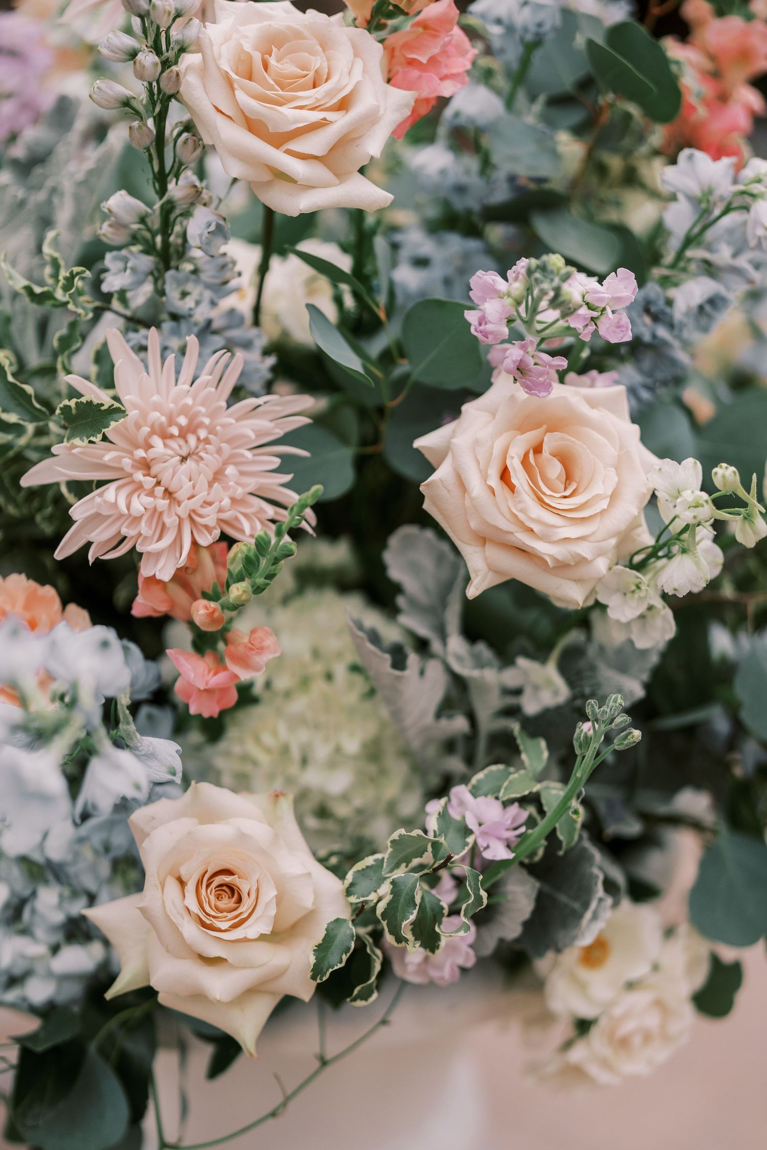 Delicate peach roses and soft pink flowers arranged with lush greenery in an elegant floral display.
